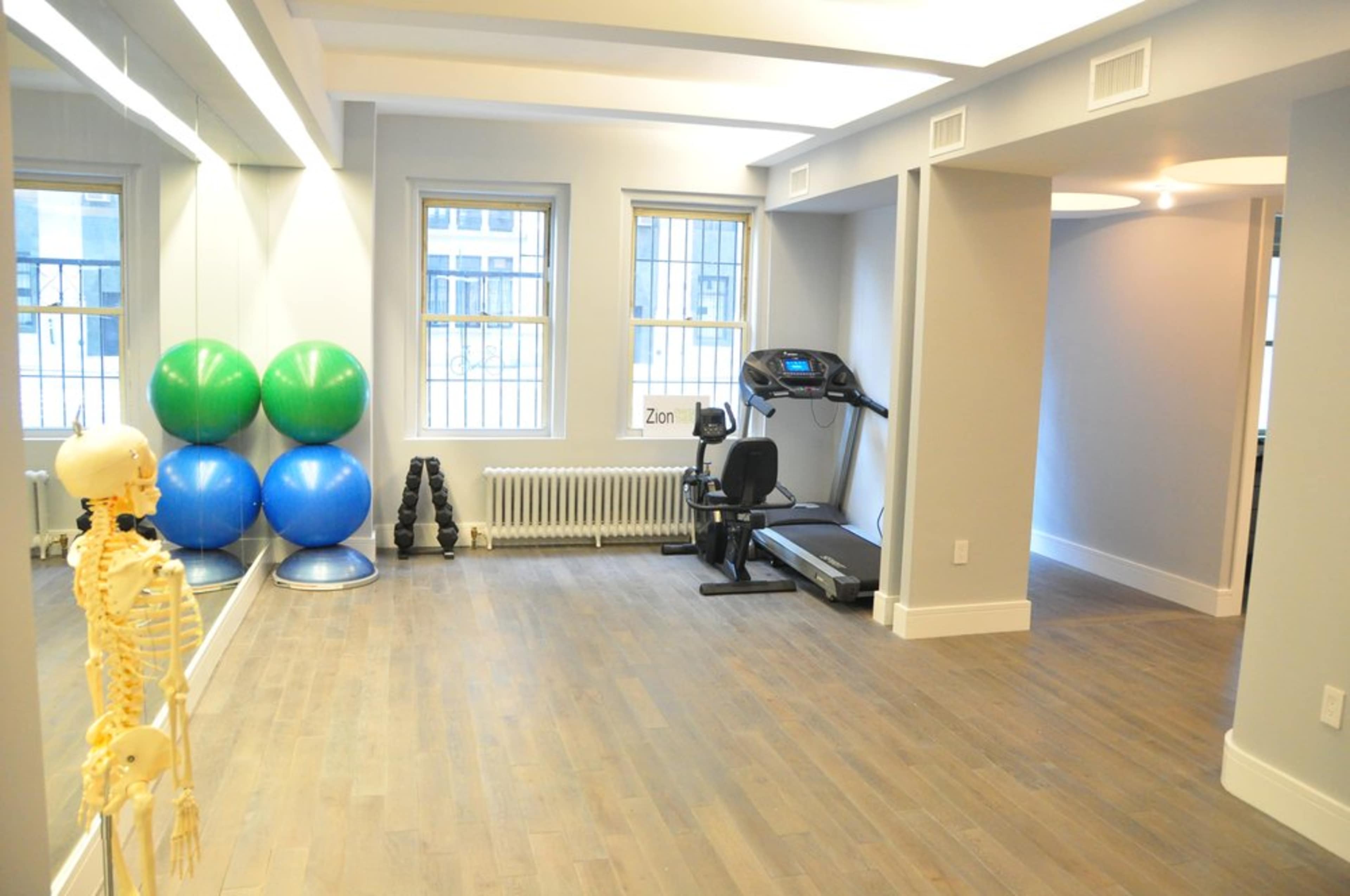 A spacious, well-lit exercise room featuring a treadmill, exercise balls, and workout weights.