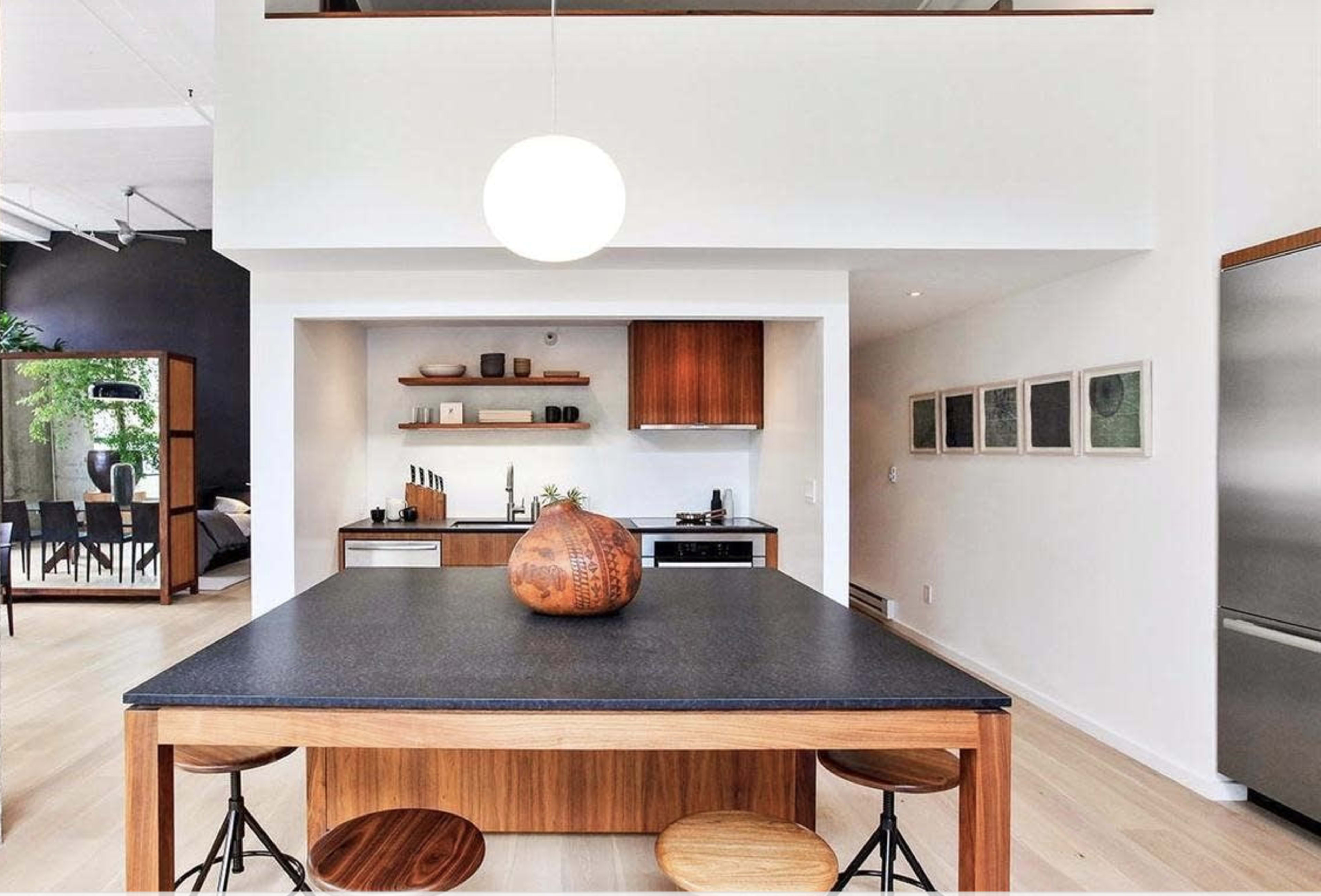 A modern kitchen with a central wooden island and a bowl on the counter, featuring open shelving and appliances in a light, airy space.
