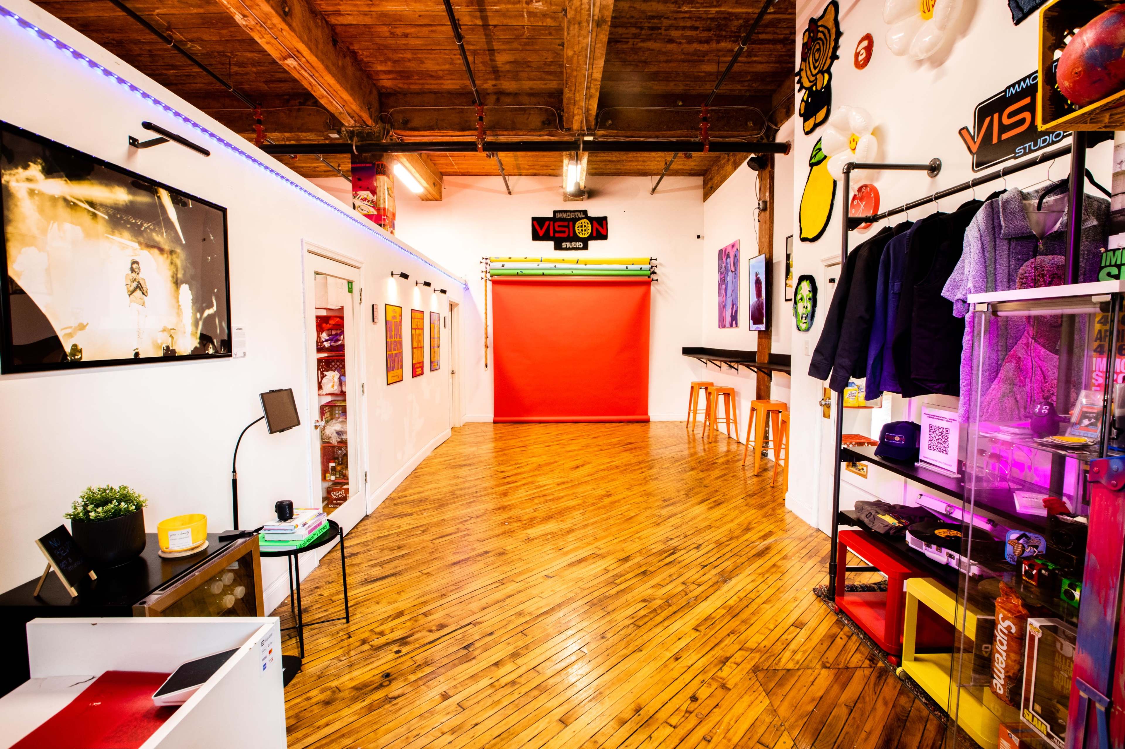A spacious studio with wooden floors features a red backdrop, colorful wall decorations, and organized display shelves.