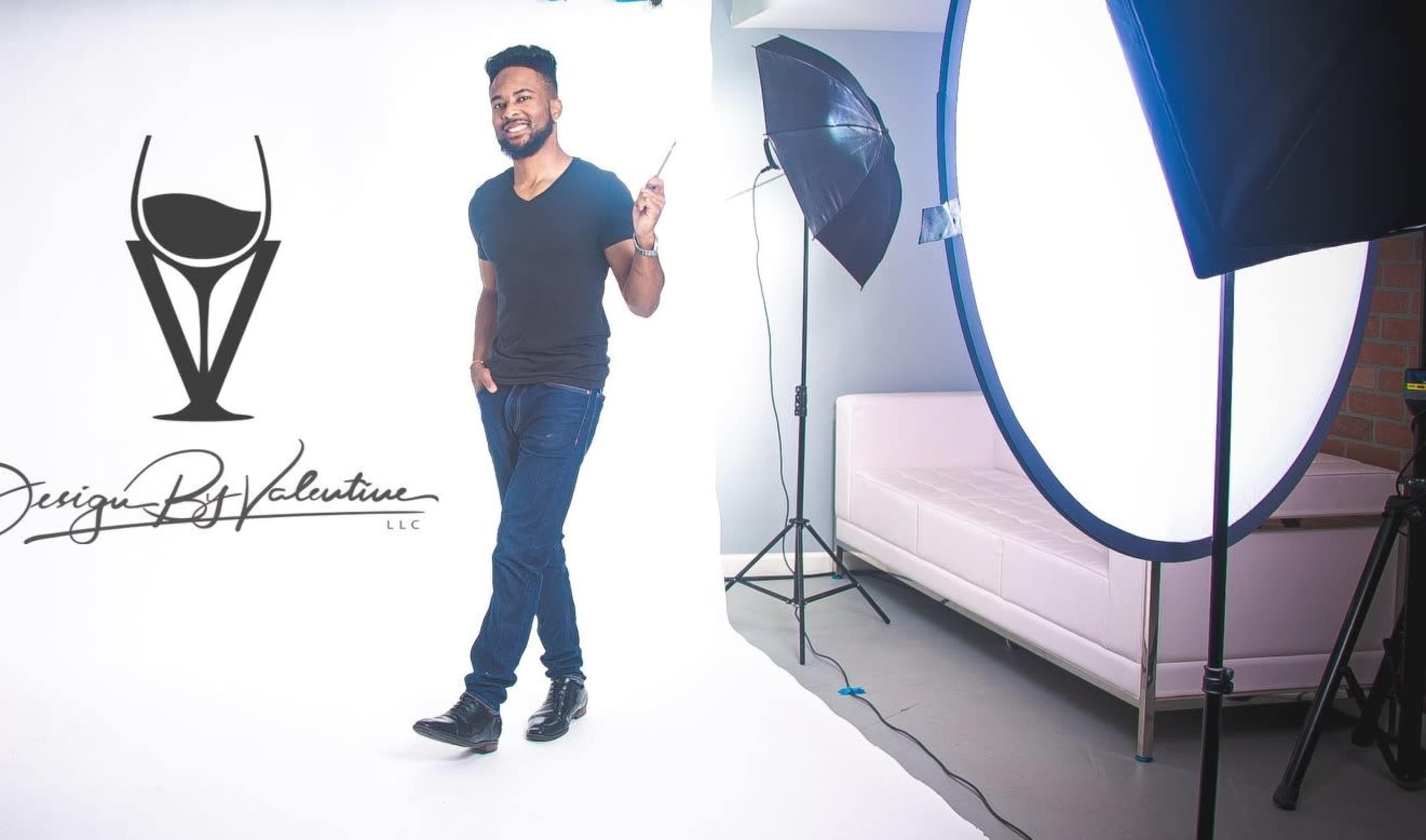 A man stands in a photography studio holding a pen, with a backdrop of white and a large light source nearby.