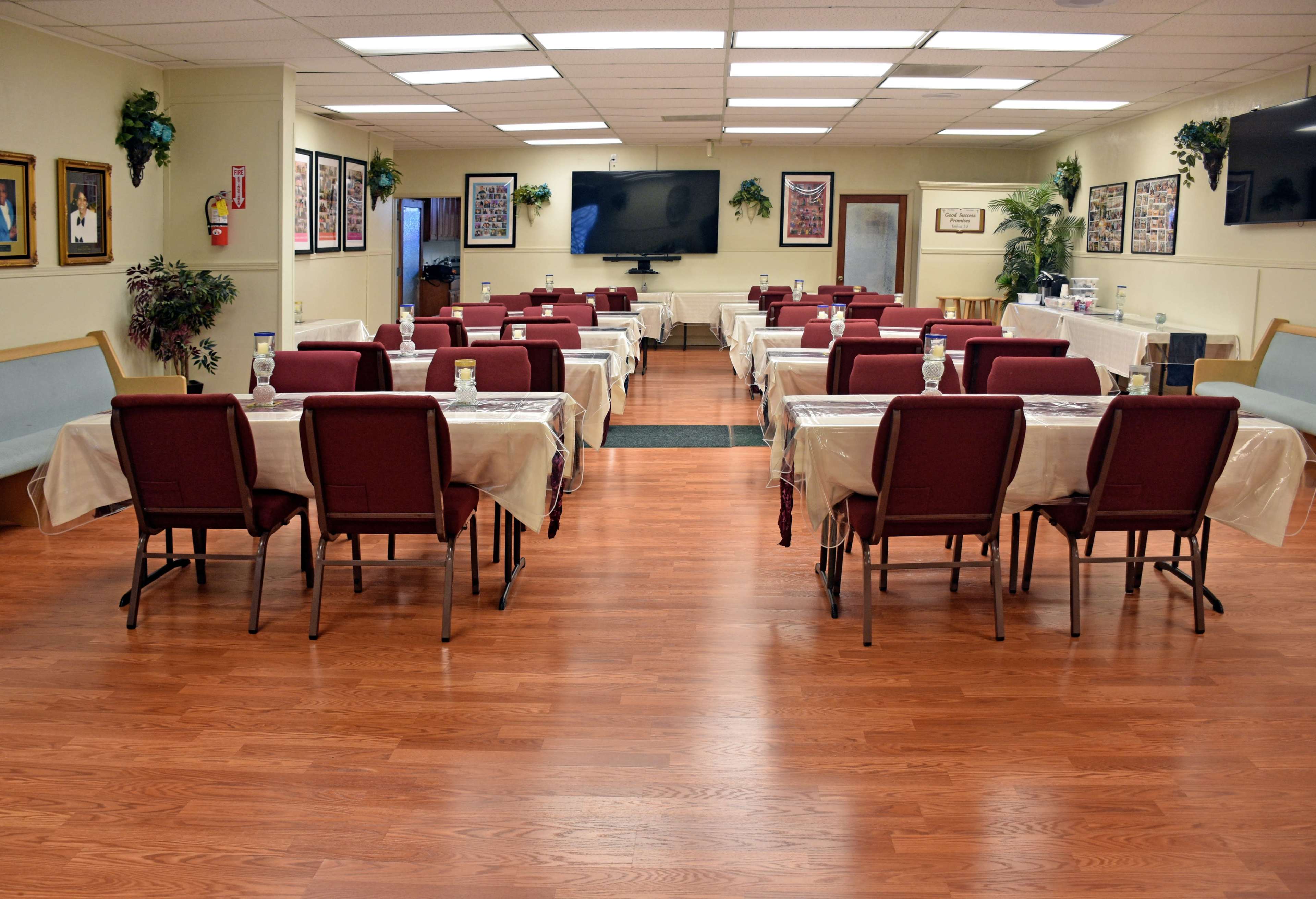 A large dining area features rows of tables covered with light-colored tablecloths and chairs arranged around them, while walls are adorned with framed photographs.