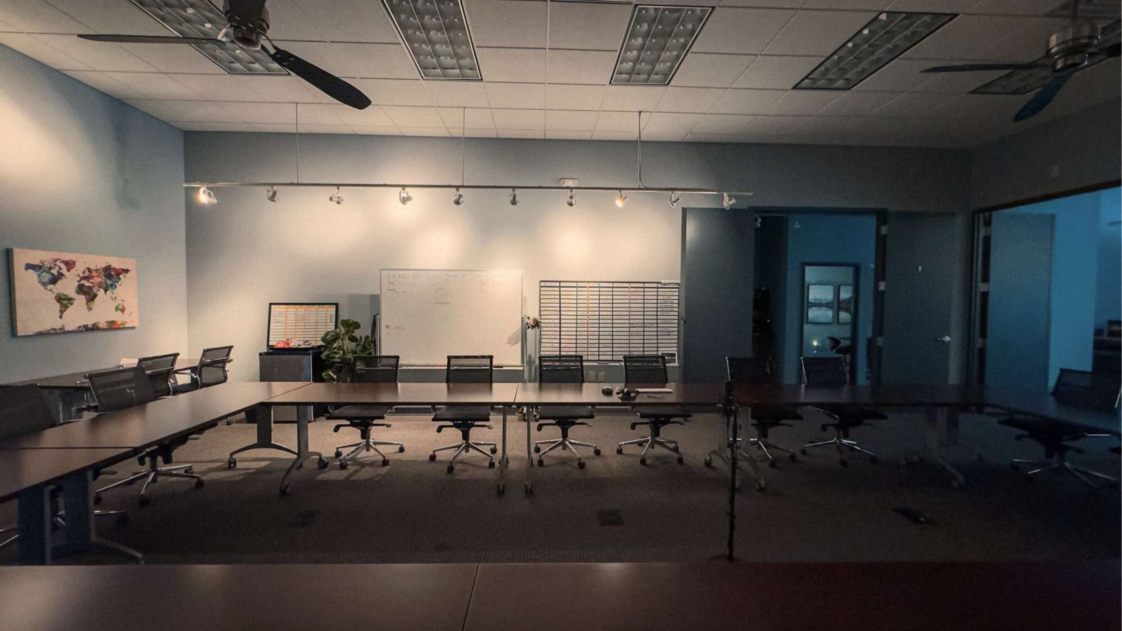 A well-lit conference room features a large table surrounded by black office chairs, a whiteboard, and a world map on the wall.