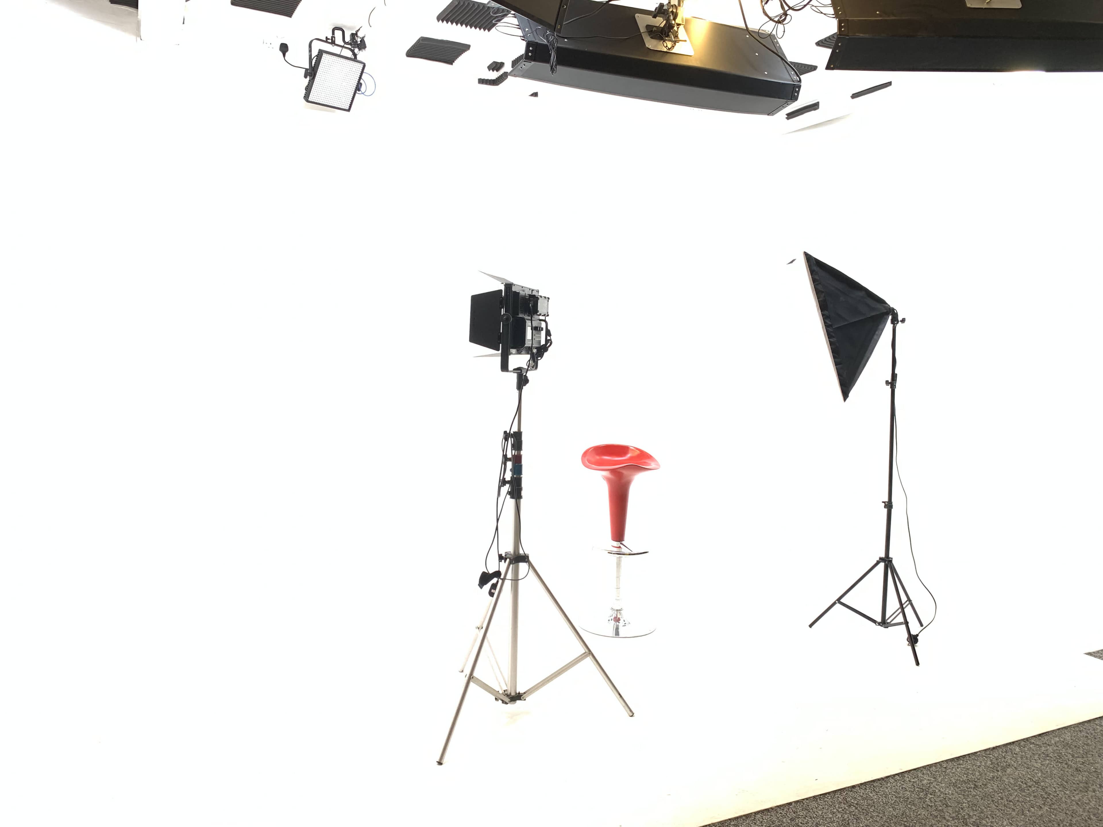A red bar stool is positioned in a brightly lit studio setup with two light stands.