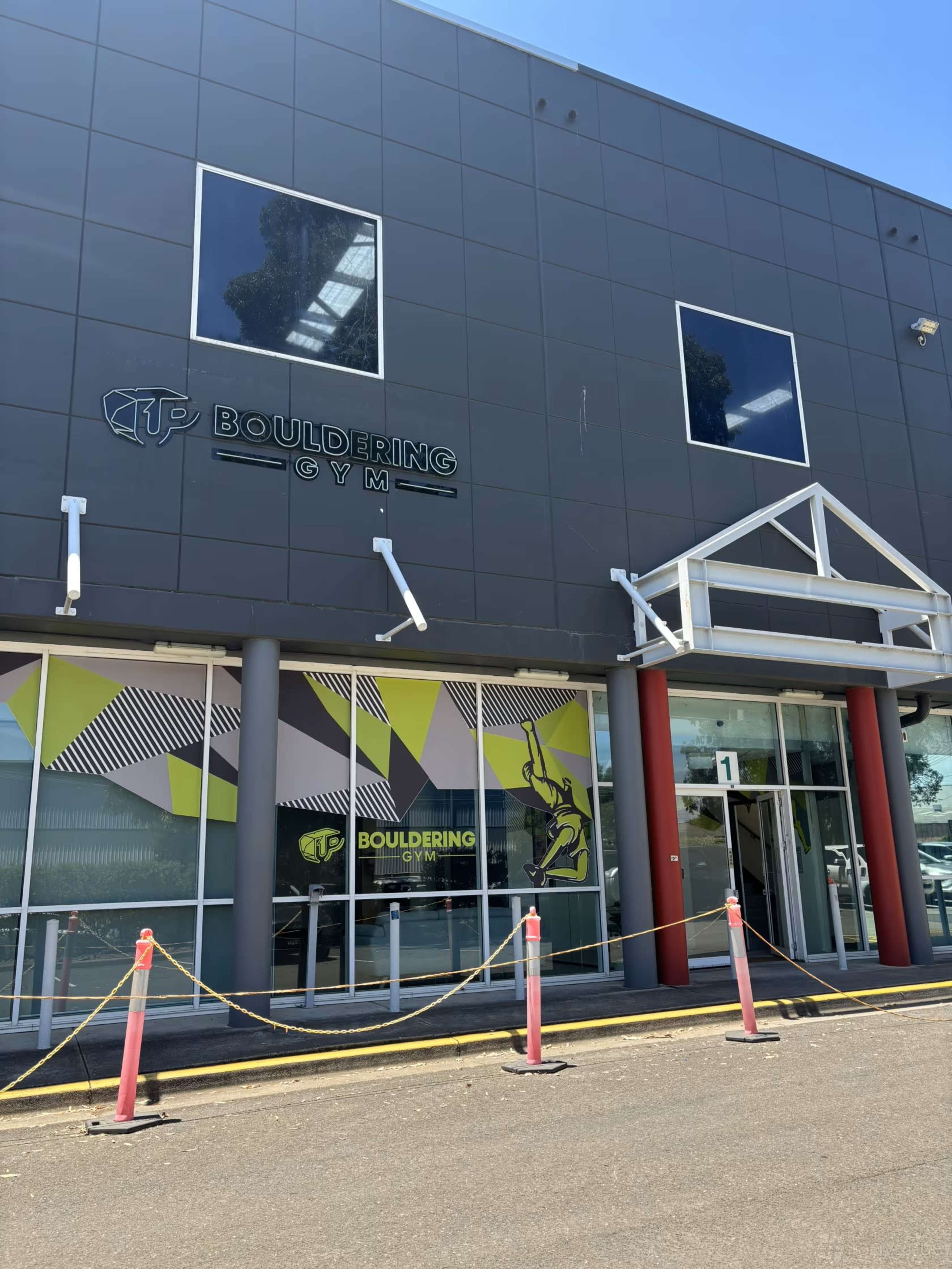The image shows the entrance of a bouldering gym with a modern façade and bright signage.