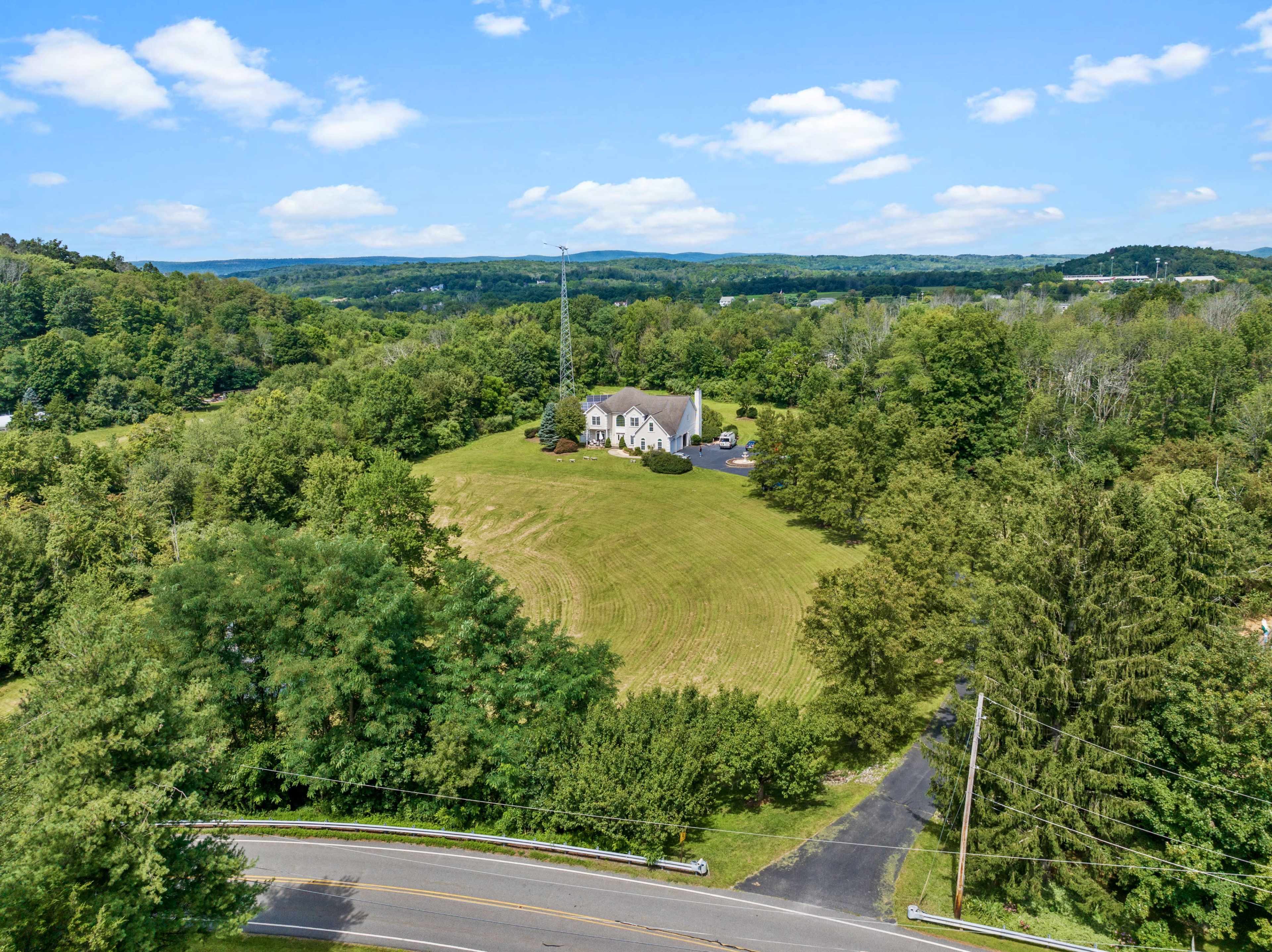 A white house is situated on a grassy hill surrounded by trees, with a winding road in the foreground.