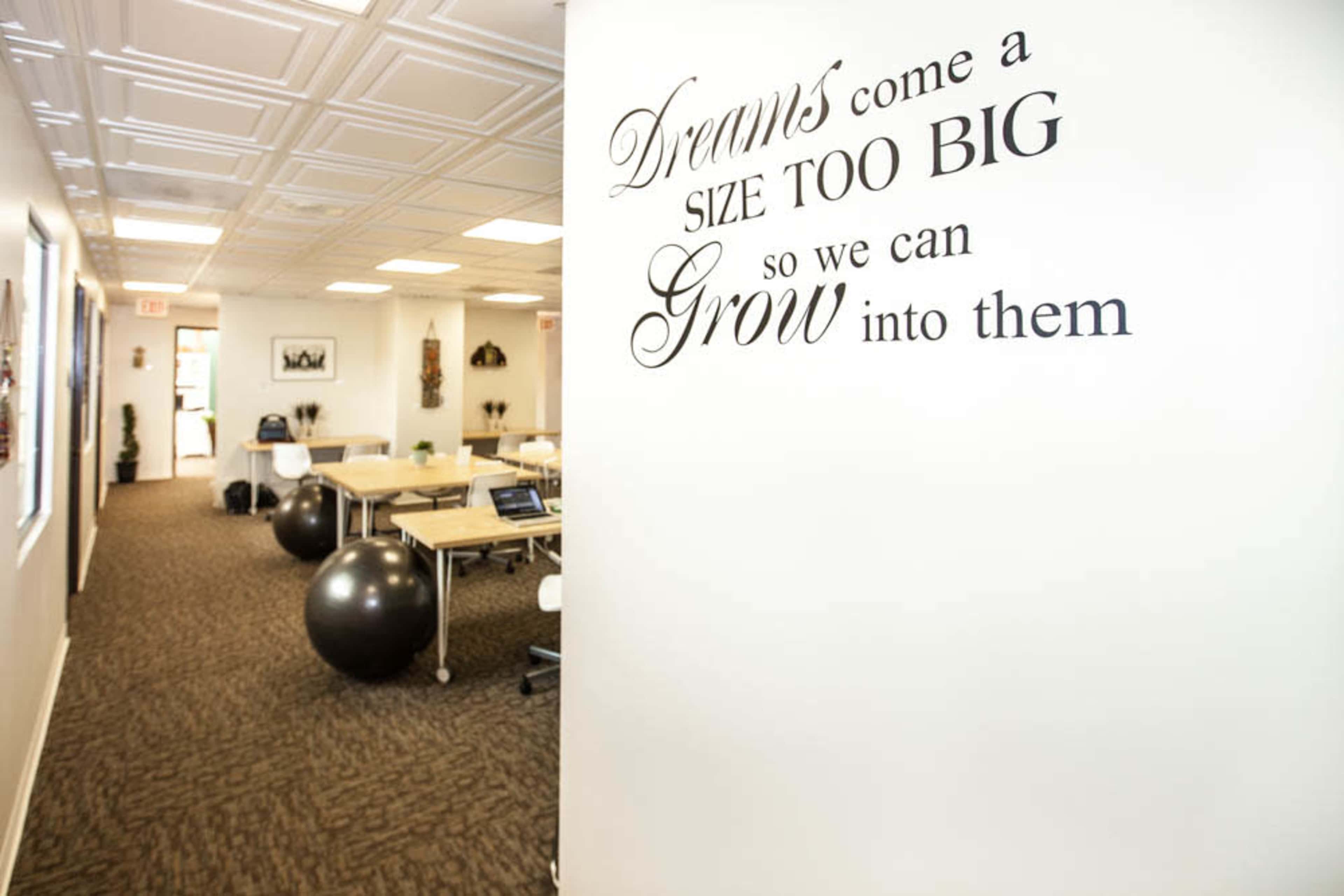 The image shows an office space with a motivational quote on the wall, desks and chairs, and exercise balls scattered throughout.
