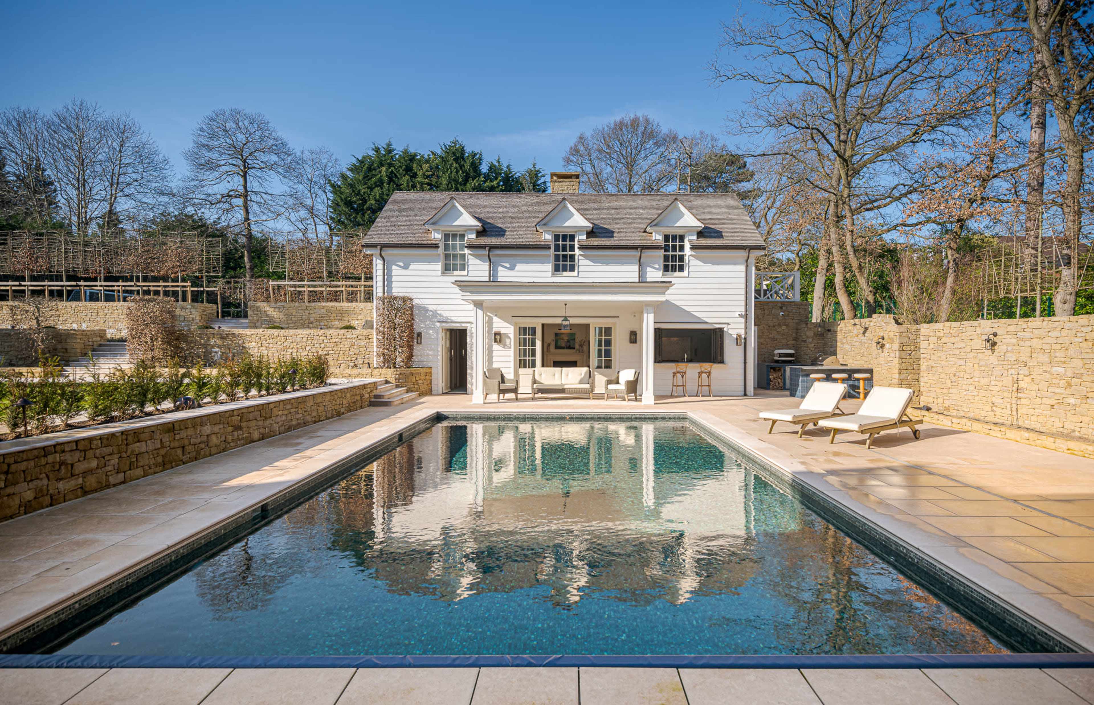A modern house with a white exterior and a large swimming pool is set in a landscaped garden.