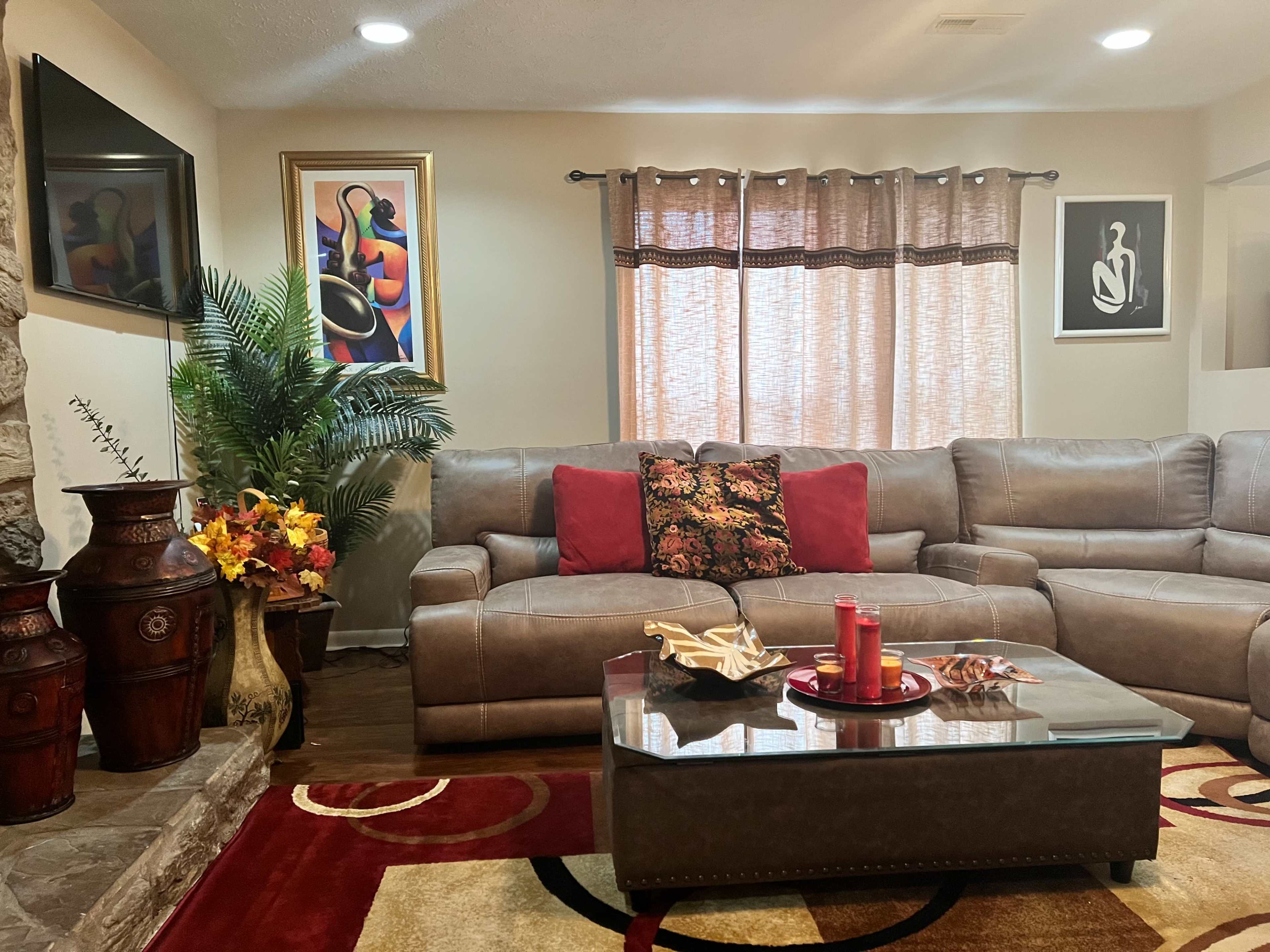 The living room features a beige sofa with red pillows, a glass coffee table, and decorative artwork on the walls, complemented by a potted plant and various decorative items.
