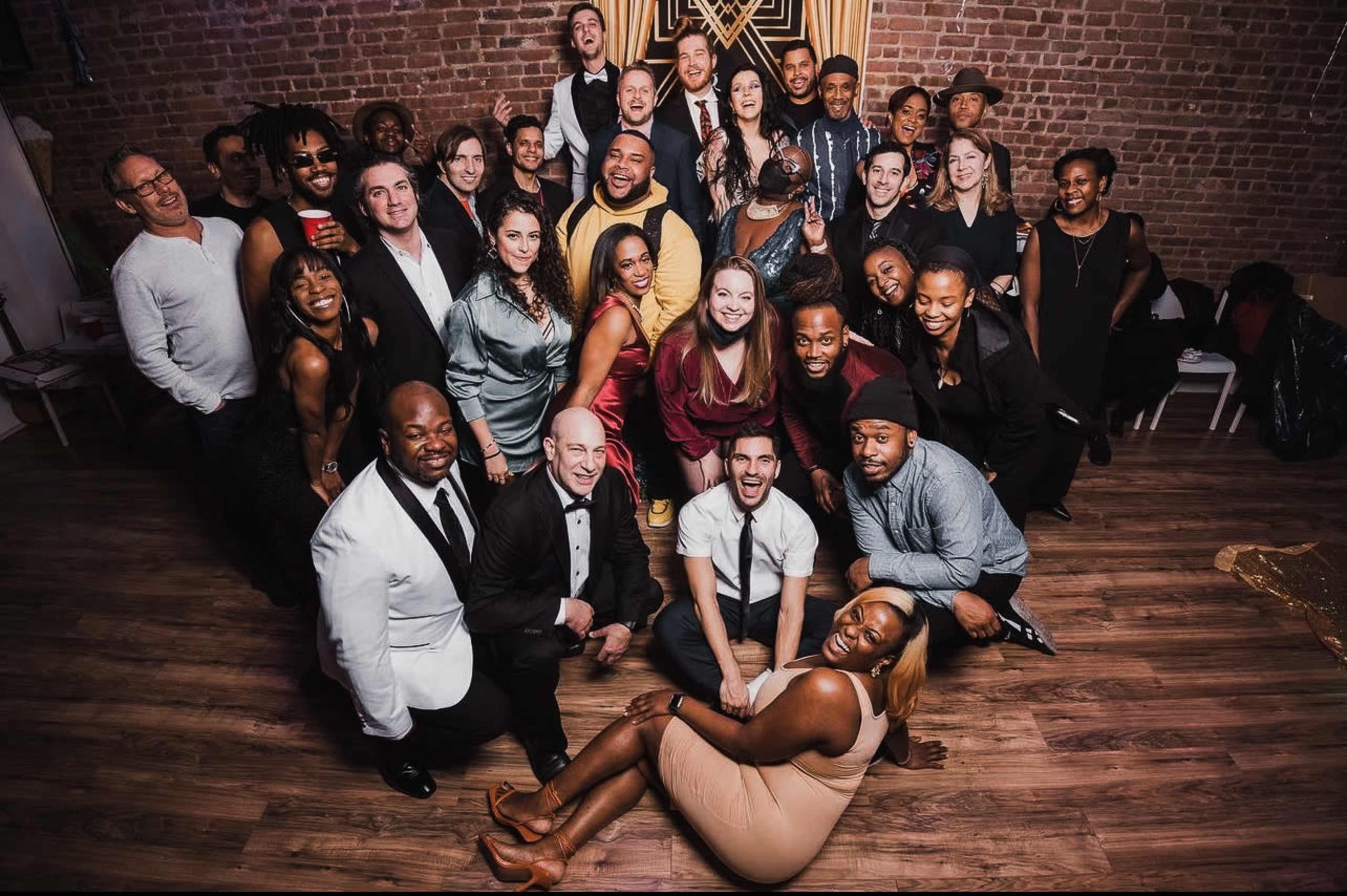 A diverse group of approximately 40 people poses together in a spacious venue with a brick wall backdrop.