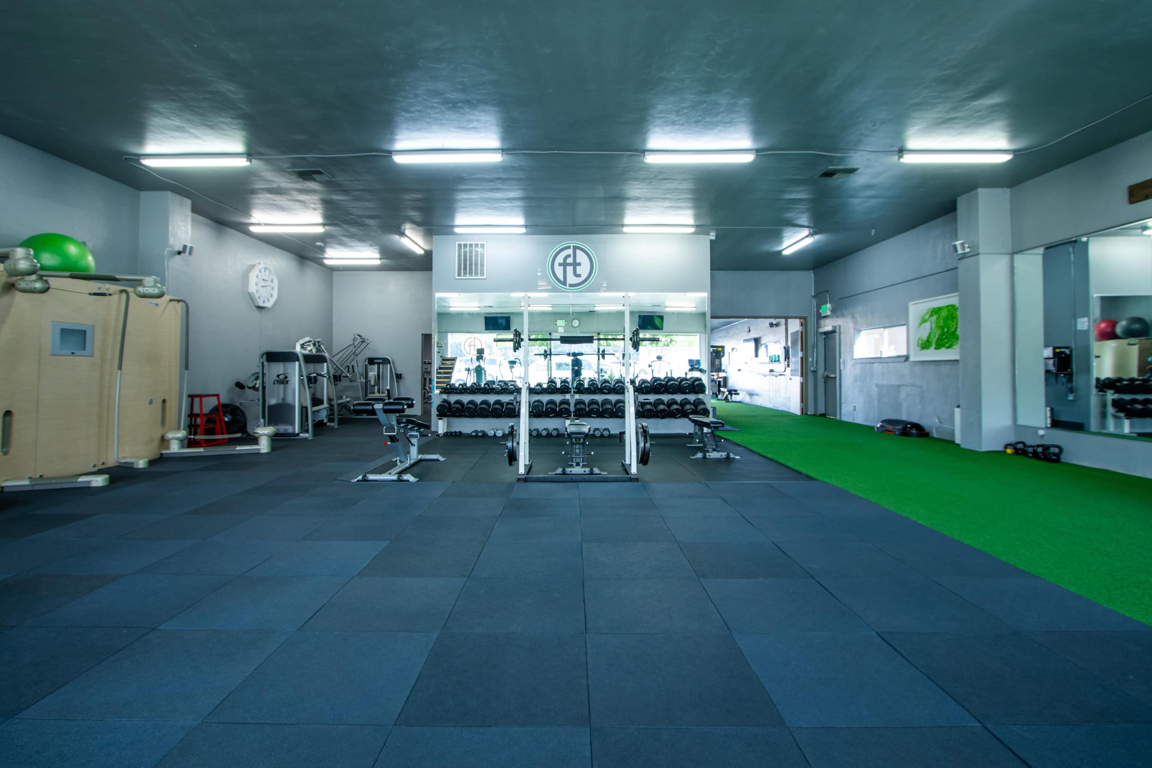 A spacious gym with workout equipment, black rubber flooring, and a green turf area.