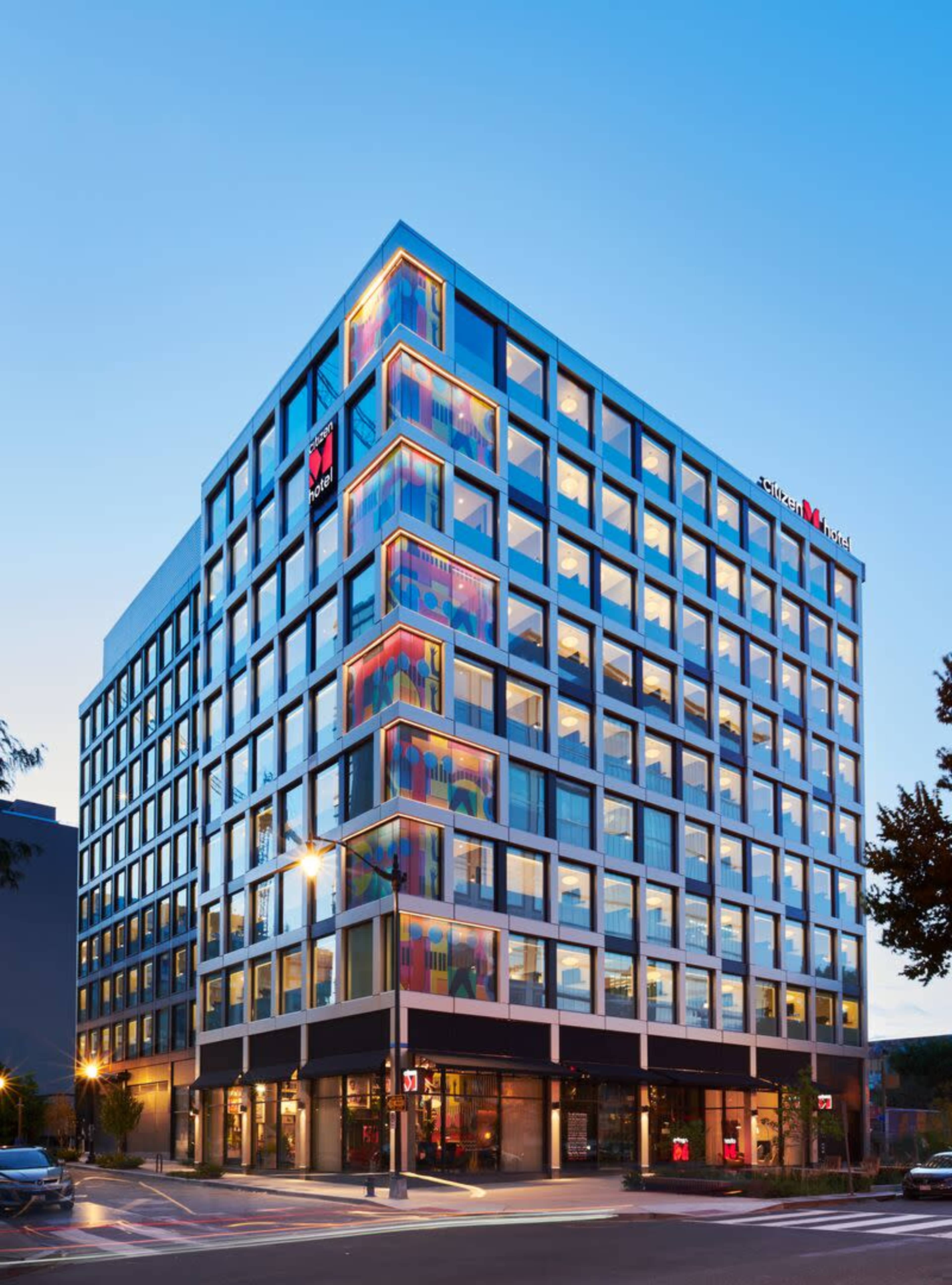 A modern multi-story hotel building with a glass facade and colorful accents at the corners, situated on a city street.