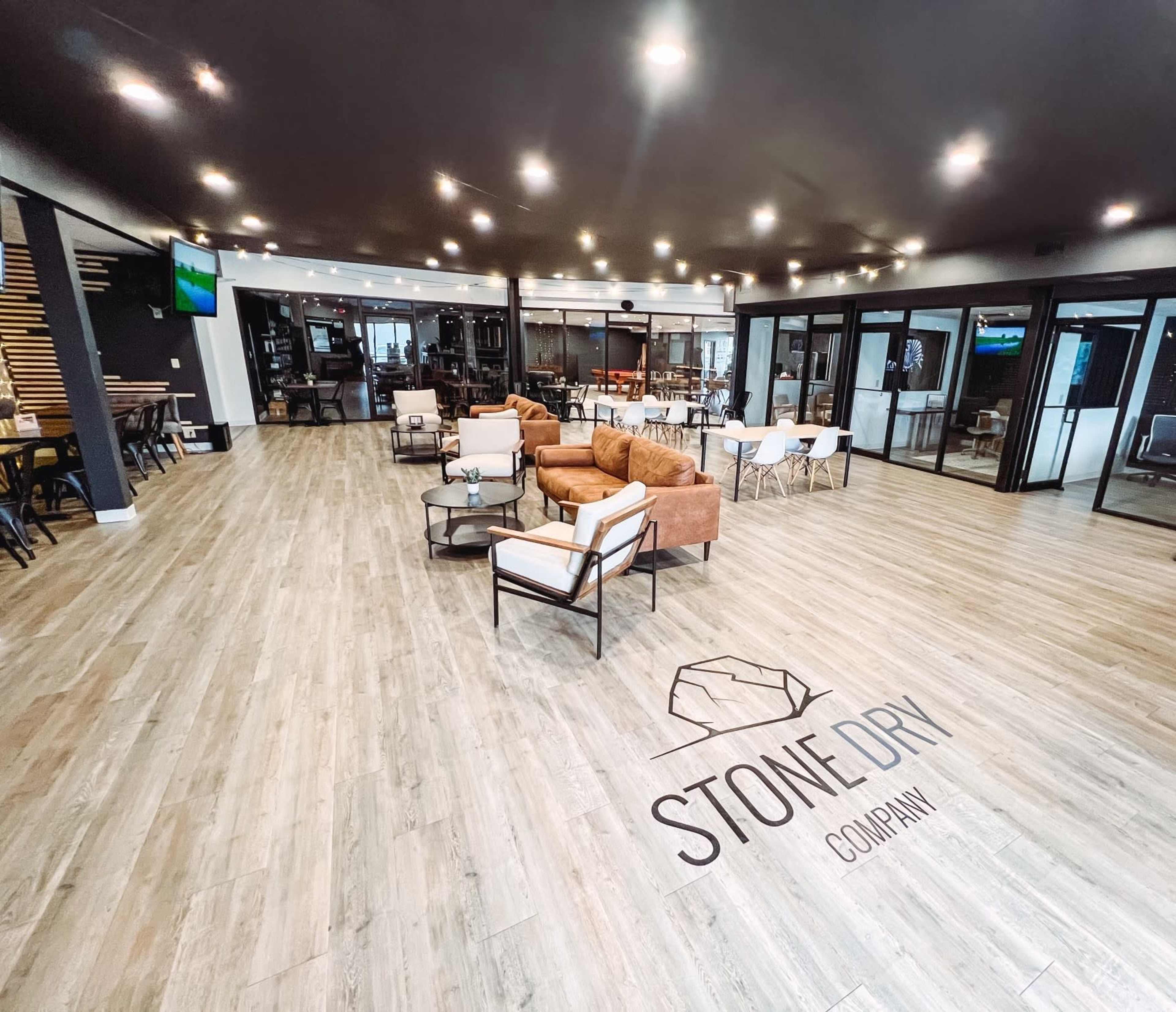 The interior of a modern office space features a seating area with brown armchairs, tables, and a large logo on the floor.