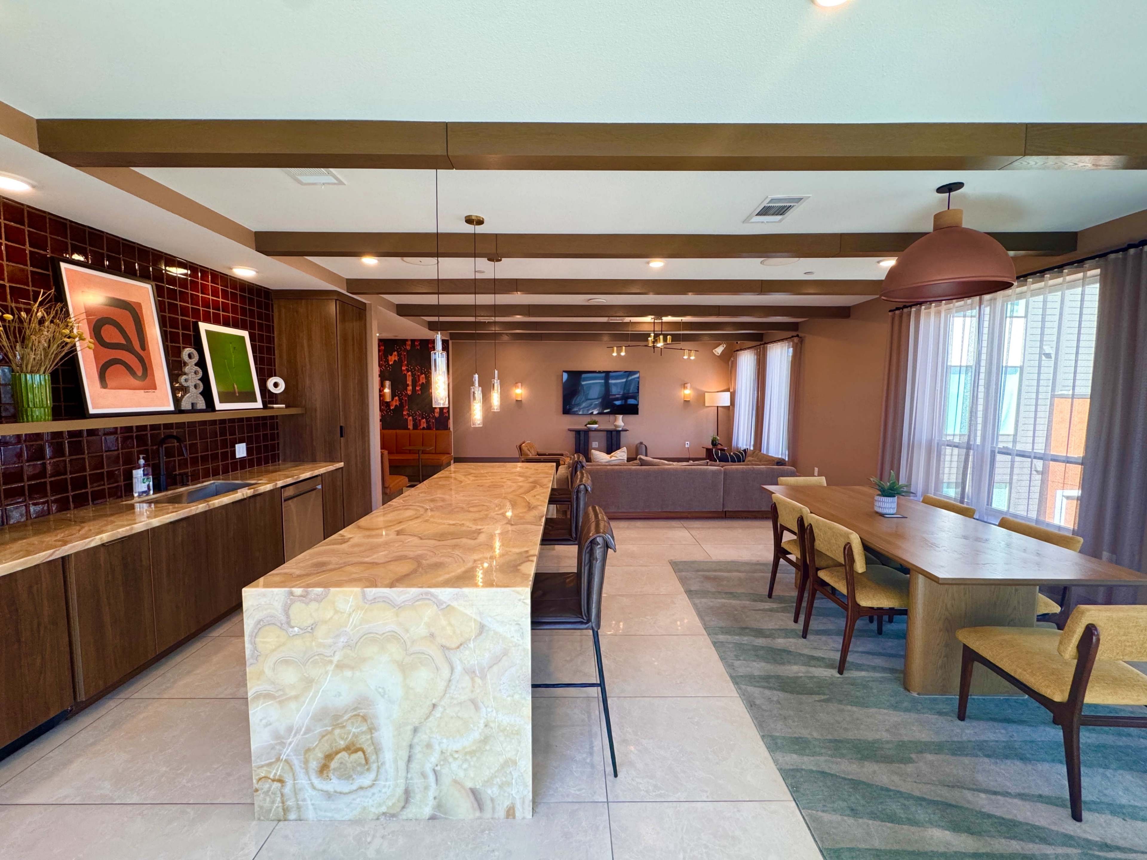 The image shows a modern open-concept living and dining area featuring a large marble countertop island, a wooden dining table with yellow chairs, and a lounge space with a television.