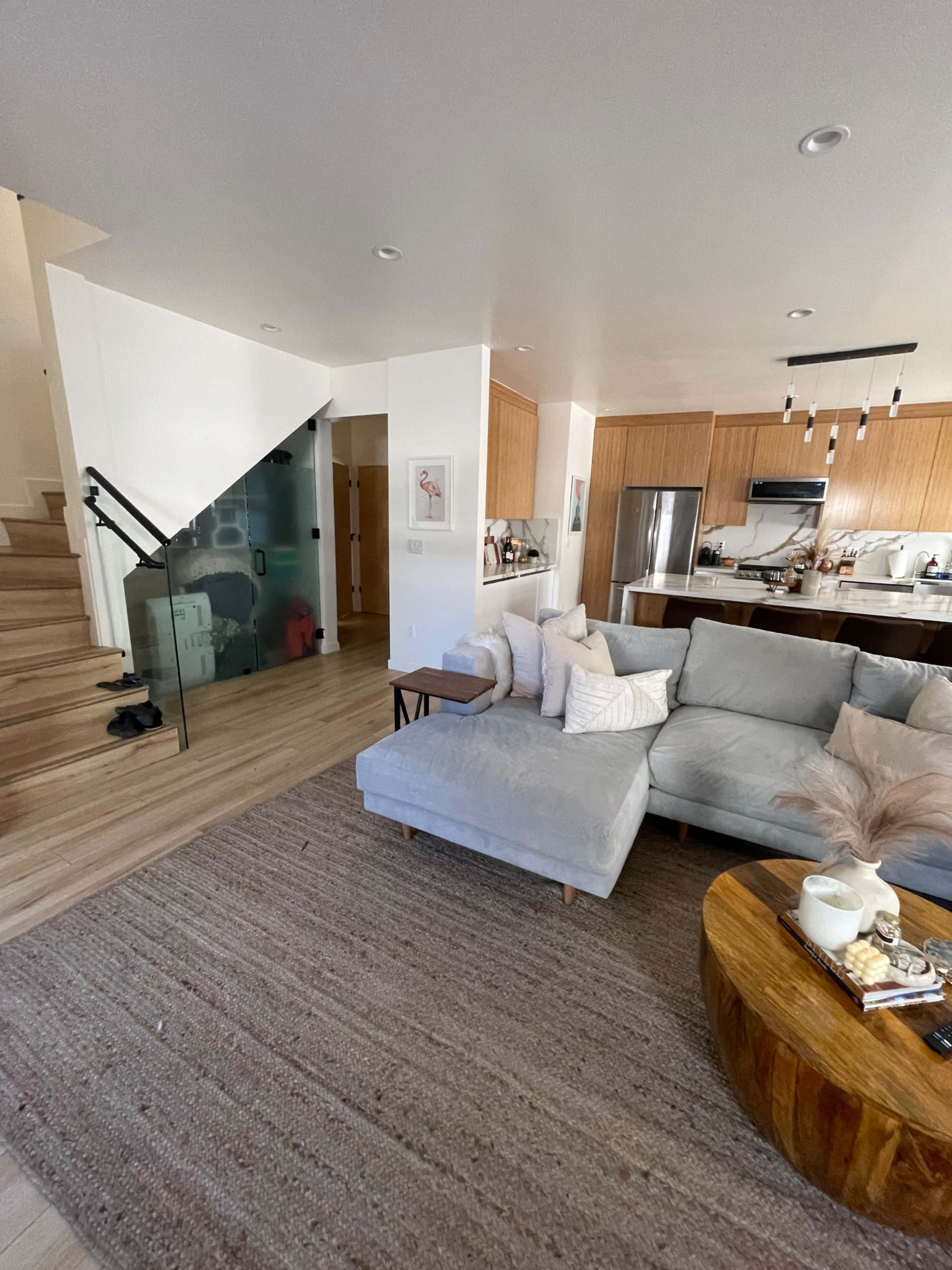 A modern living room with light-colored furniture, a wooden coffee table, and a staircase leading to an upper level.