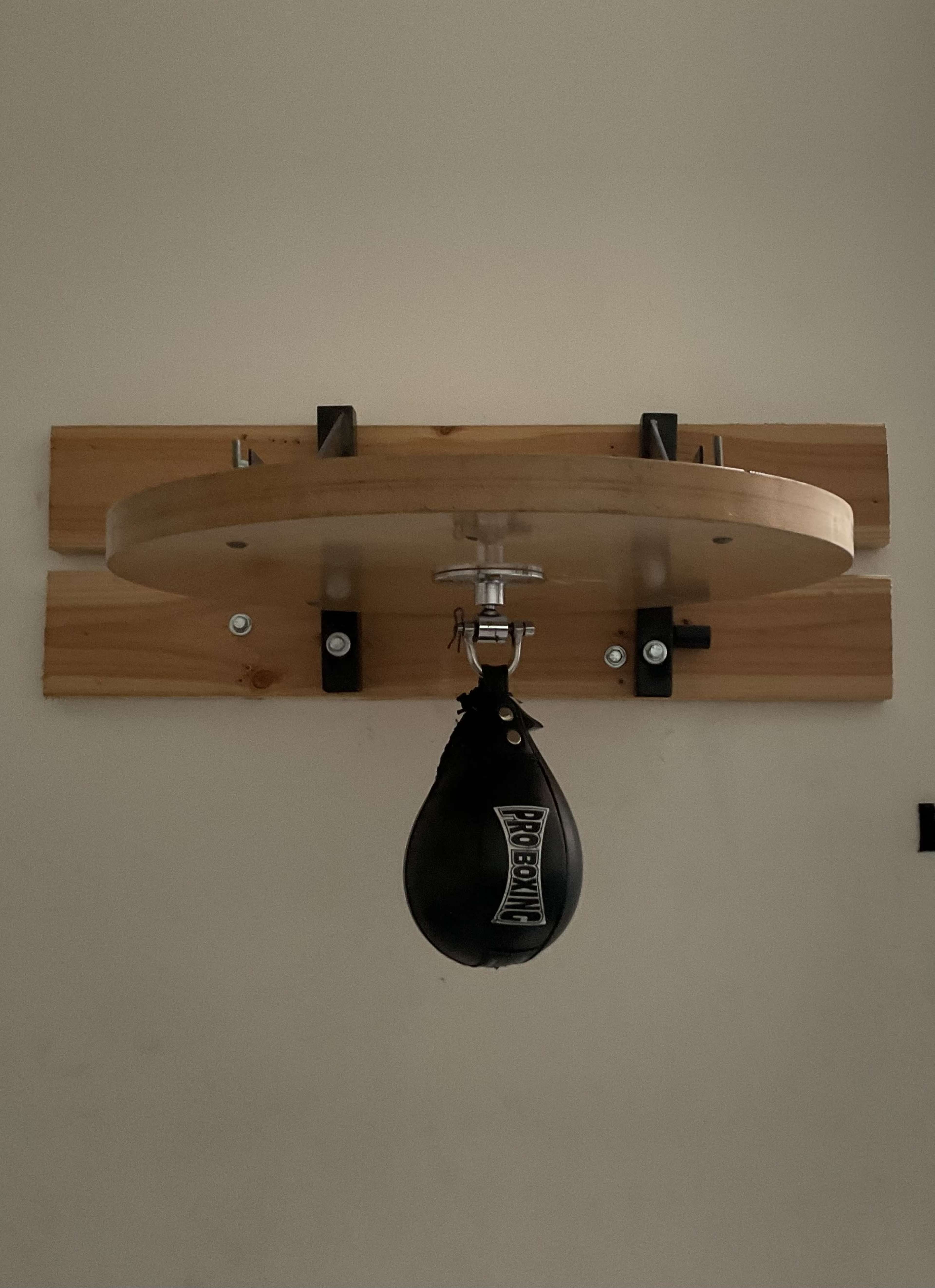 A hanging speed bag is mounted on a wooden platform secured to a wall.