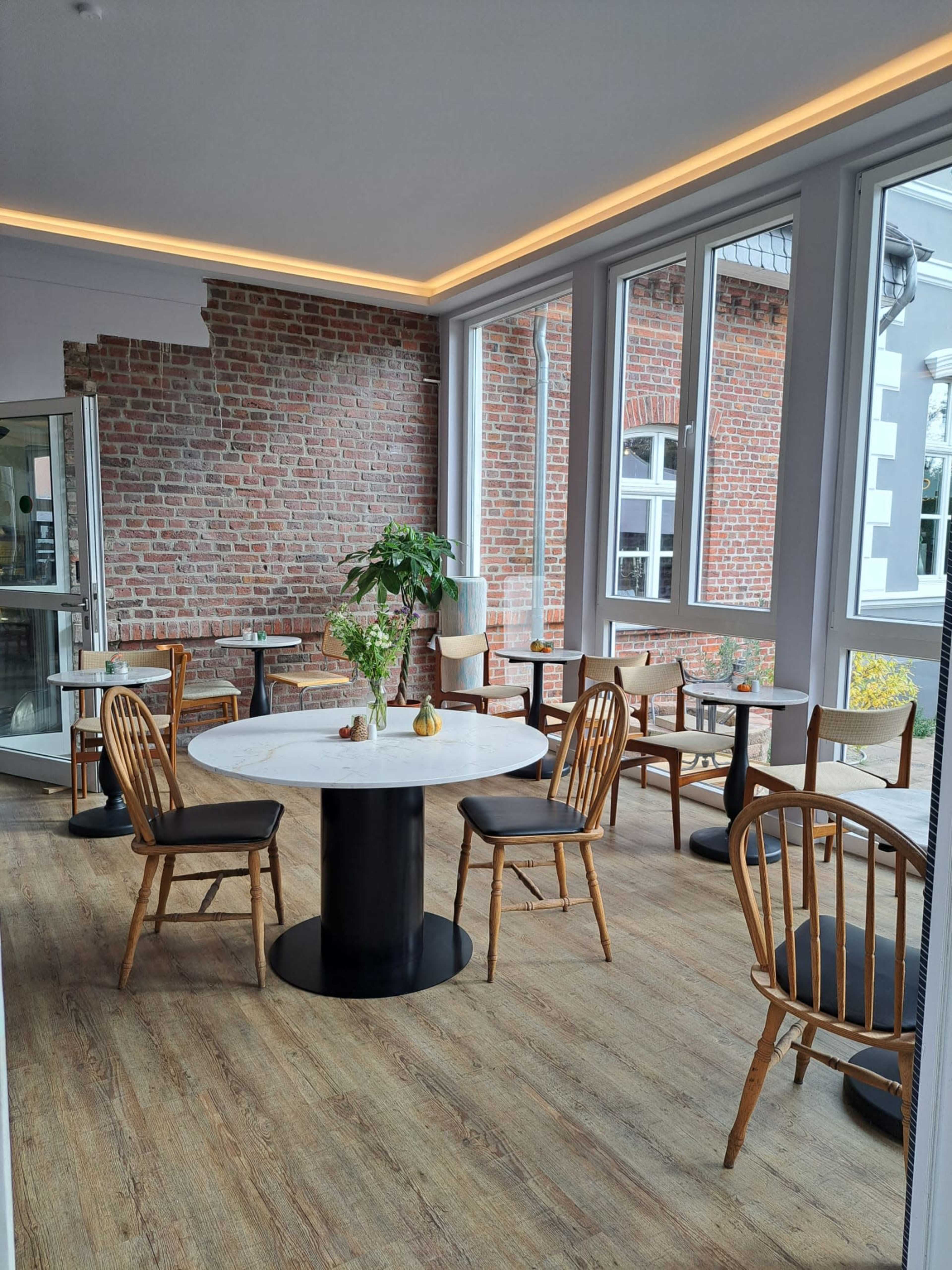 A modern café interior with wooden chairs, round tables, and a brick wall.