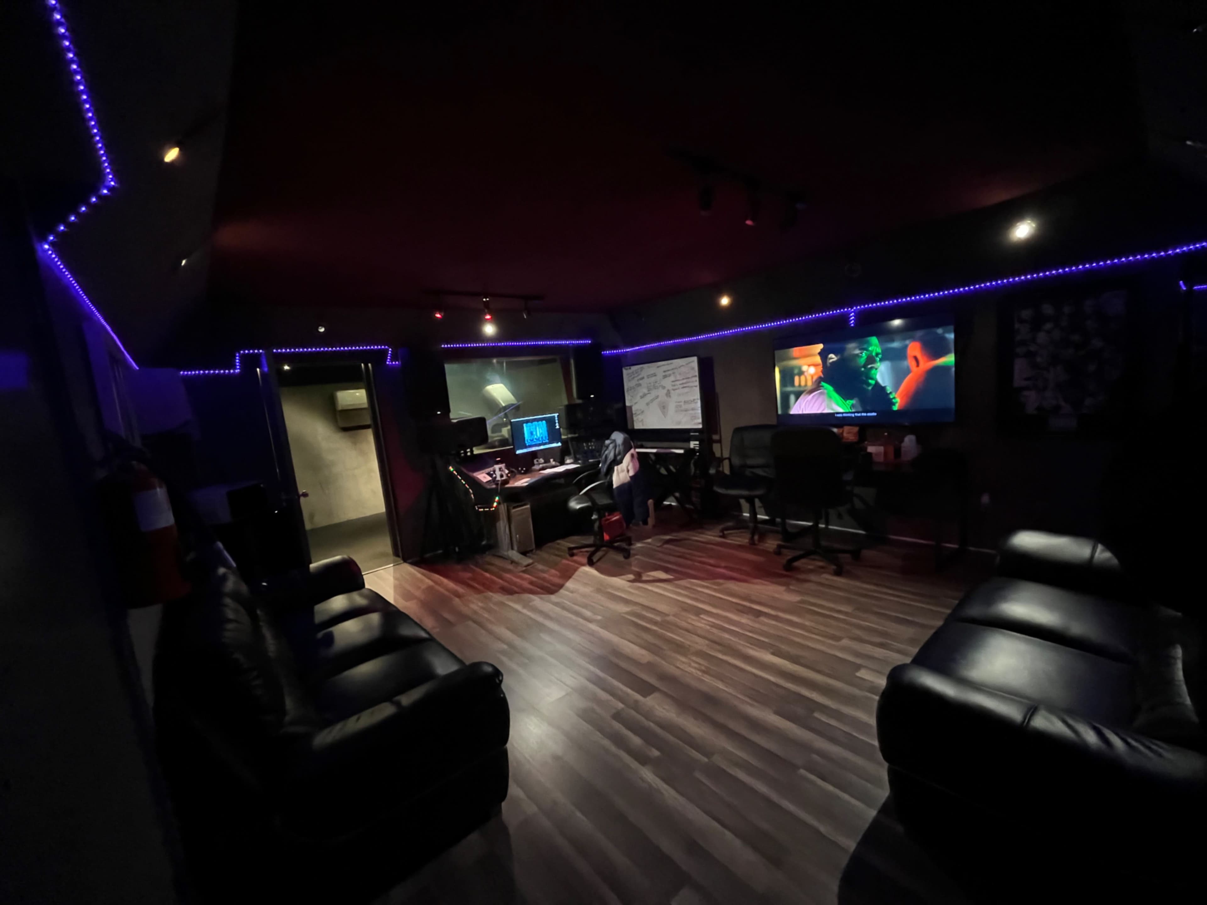 A recording studio with dark walls, a central control area, and dim lighting accented by purple LED strips.