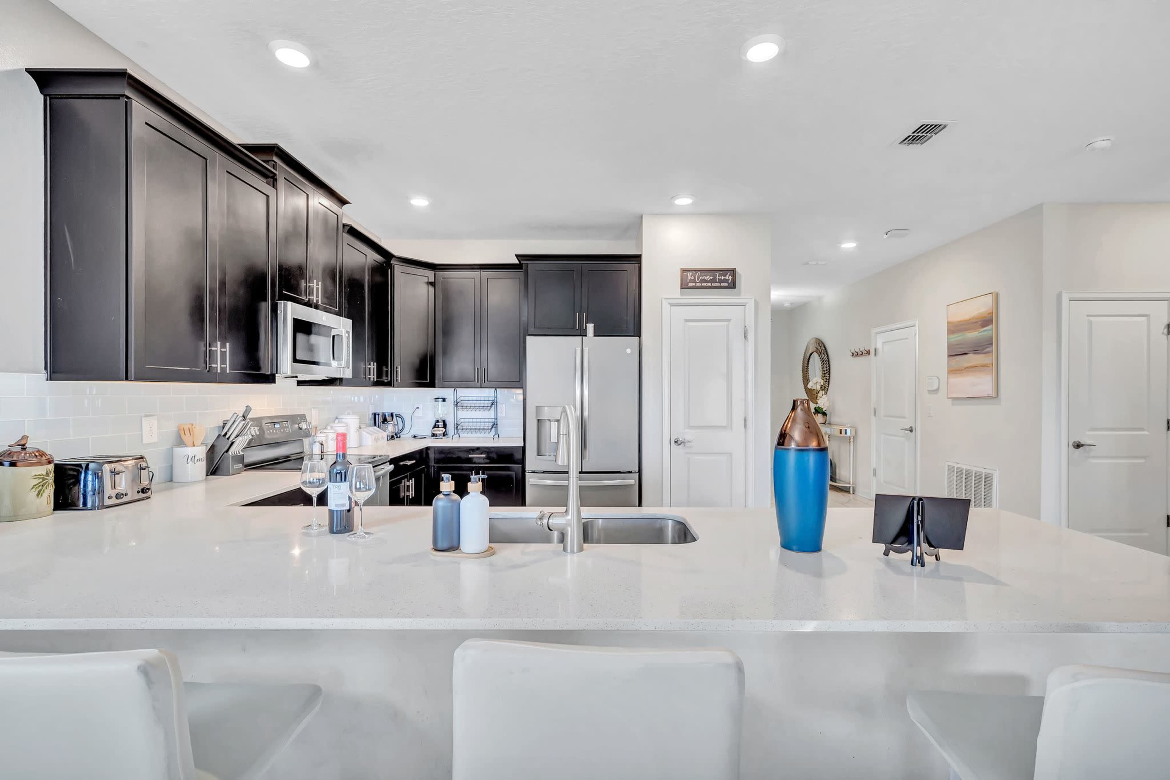 A modern kitchen with dark cabinetry, stainless steel appliances, and a white countertop with bar seating.