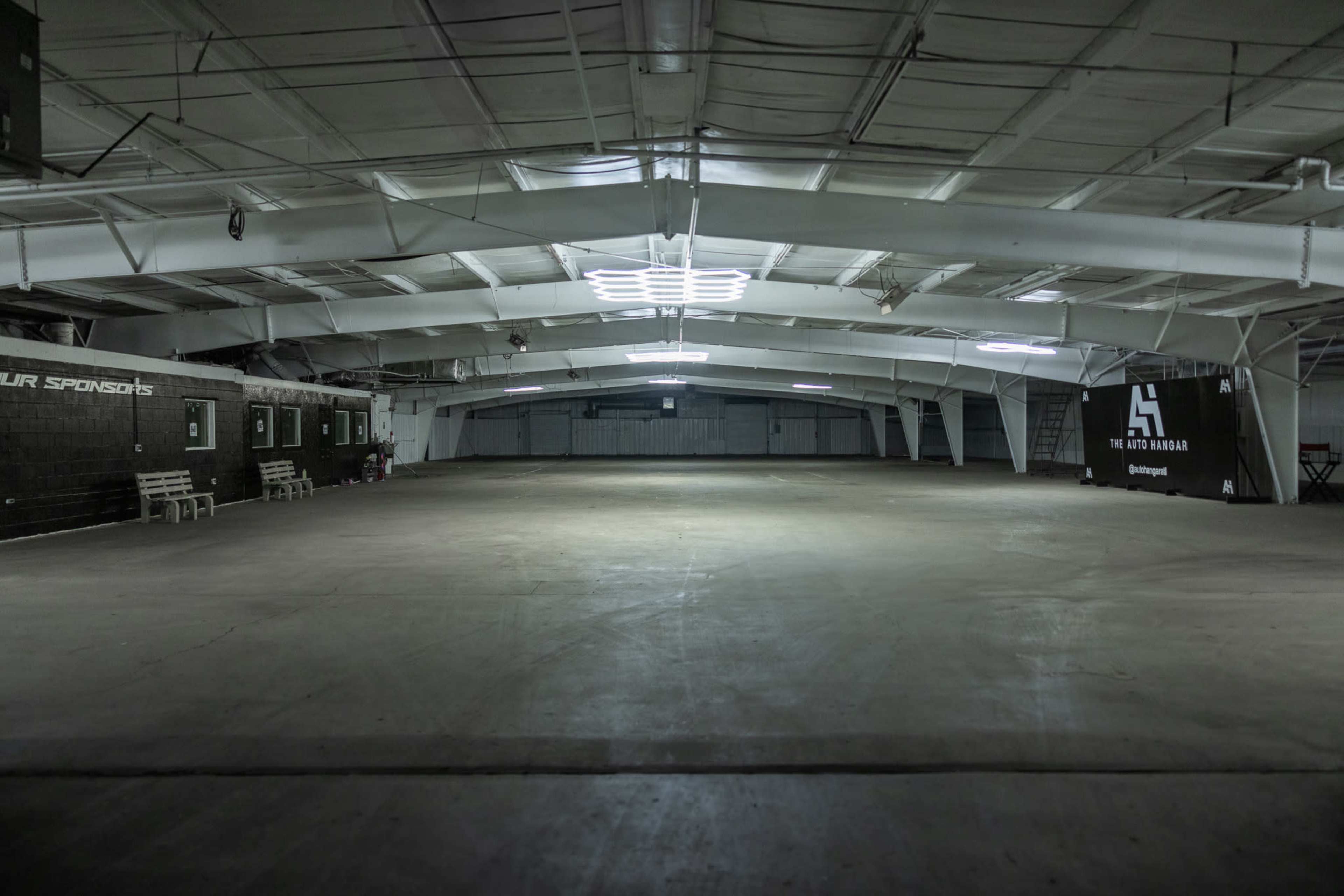 The image shows a spacious, empty indoor warehouse with metal beams and a concrete floor.
