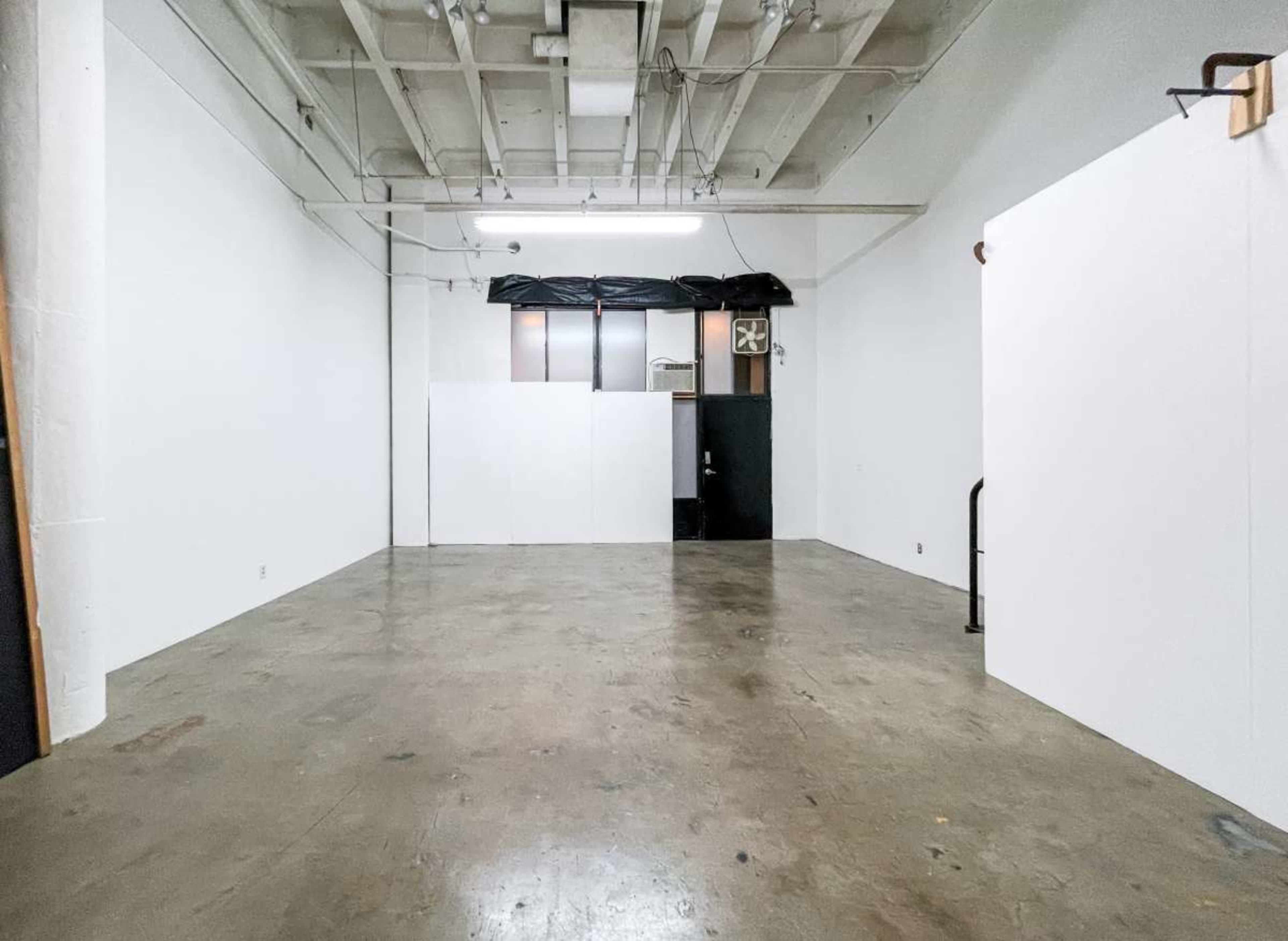 The image shows a spacious, empty interior of a room with concrete flooring and white walls.