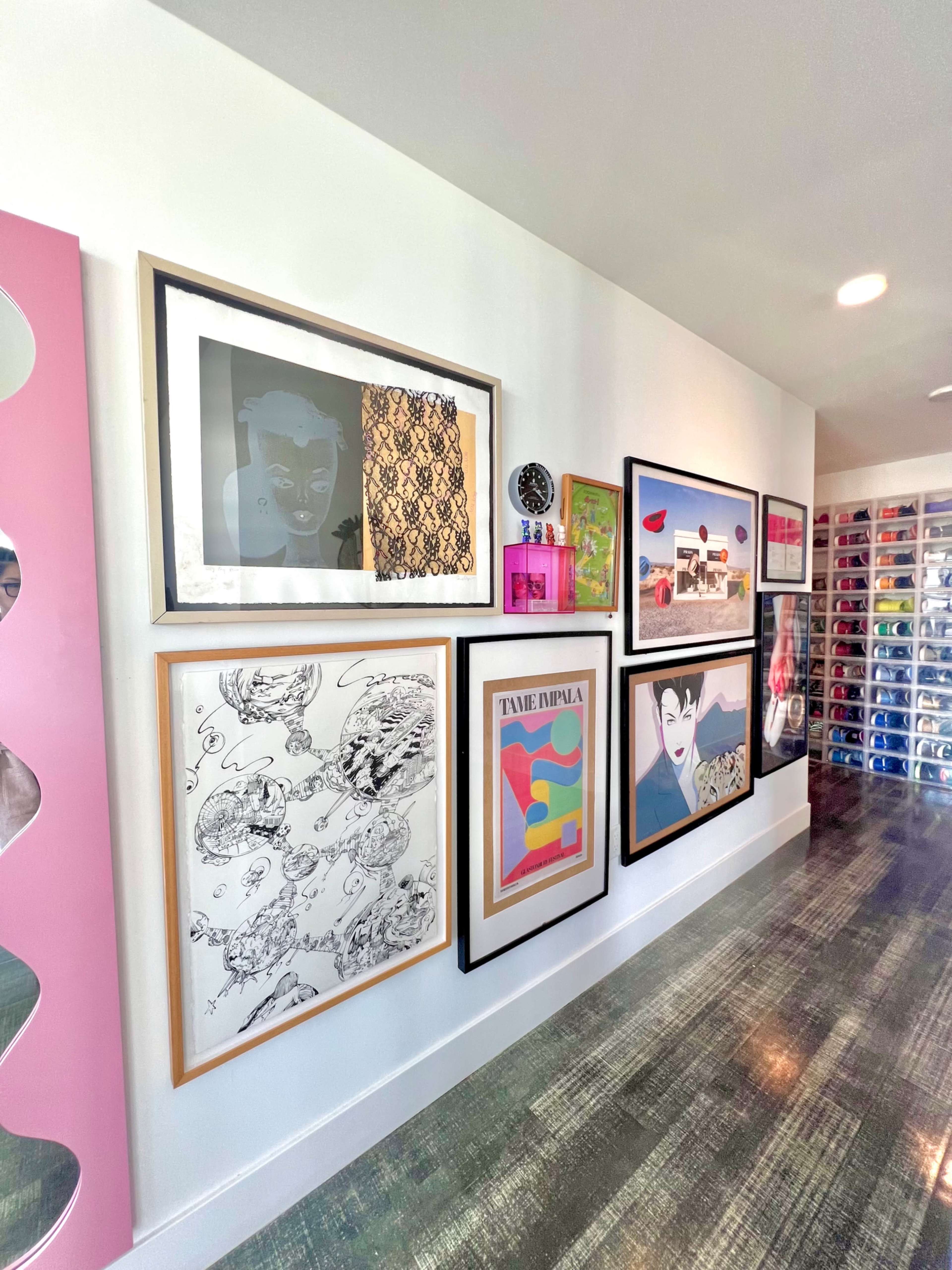 The image shows a brightly lit room with a wall featuring a gallery of framed artwork, including prints and photographs, alongside a section with colorful shoe storage.