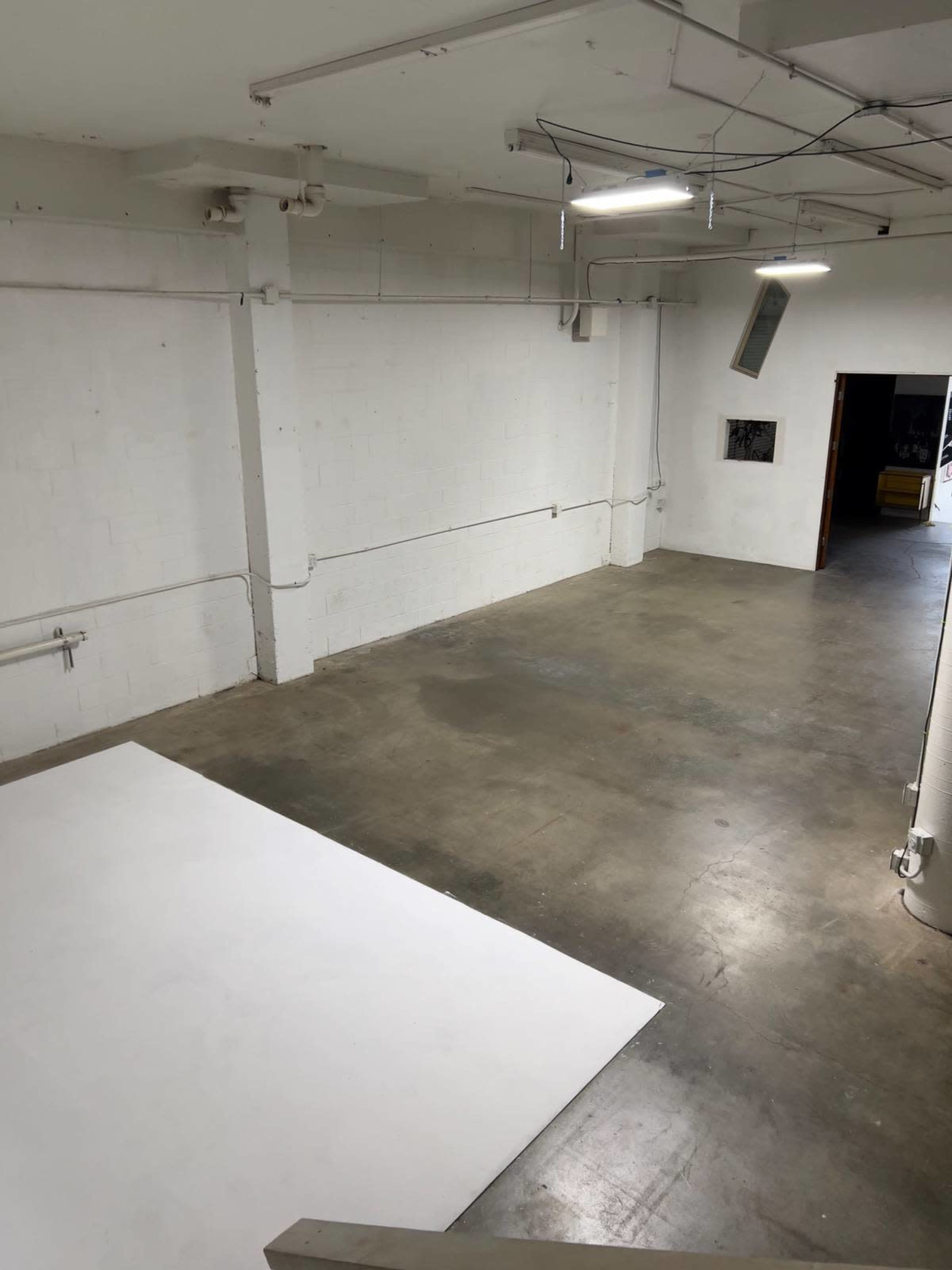 The image shows an empty studio space with concrete flooring and a large white area at the center.
