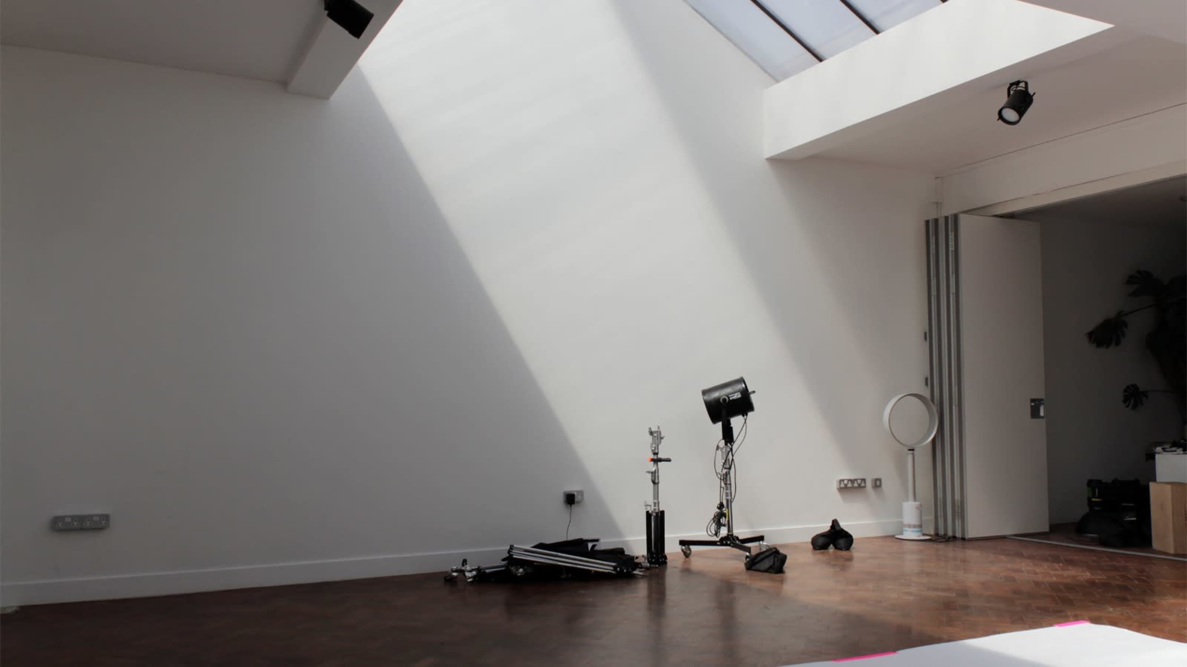 A beam of natural light streams down from a skylight onto a sparsely furnished room with wooden flooring and a few equipment items in the corner.