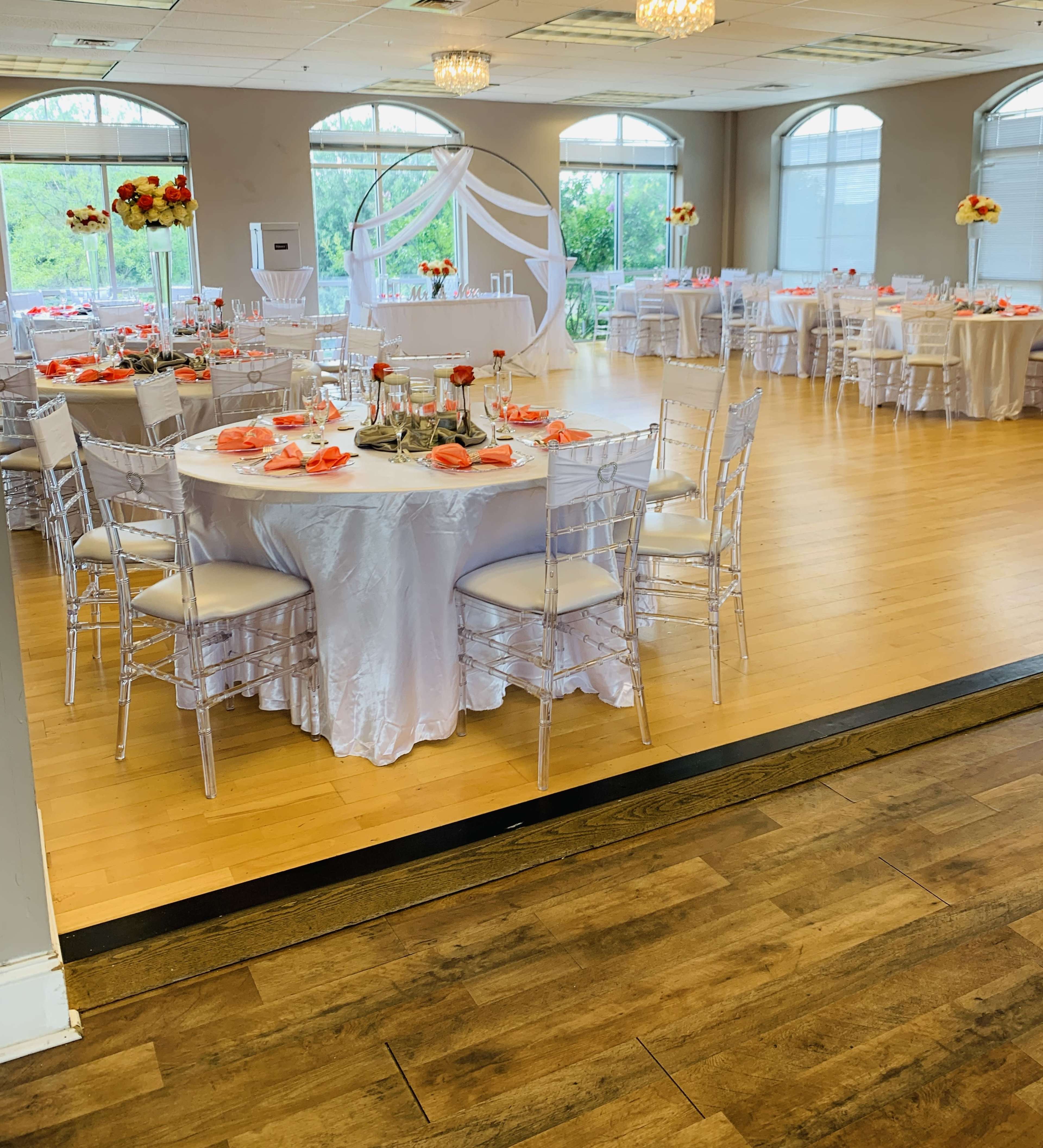 A decorated banquet room features round tables set with white tablecloths, elegant chairs, and floral centerpieces.