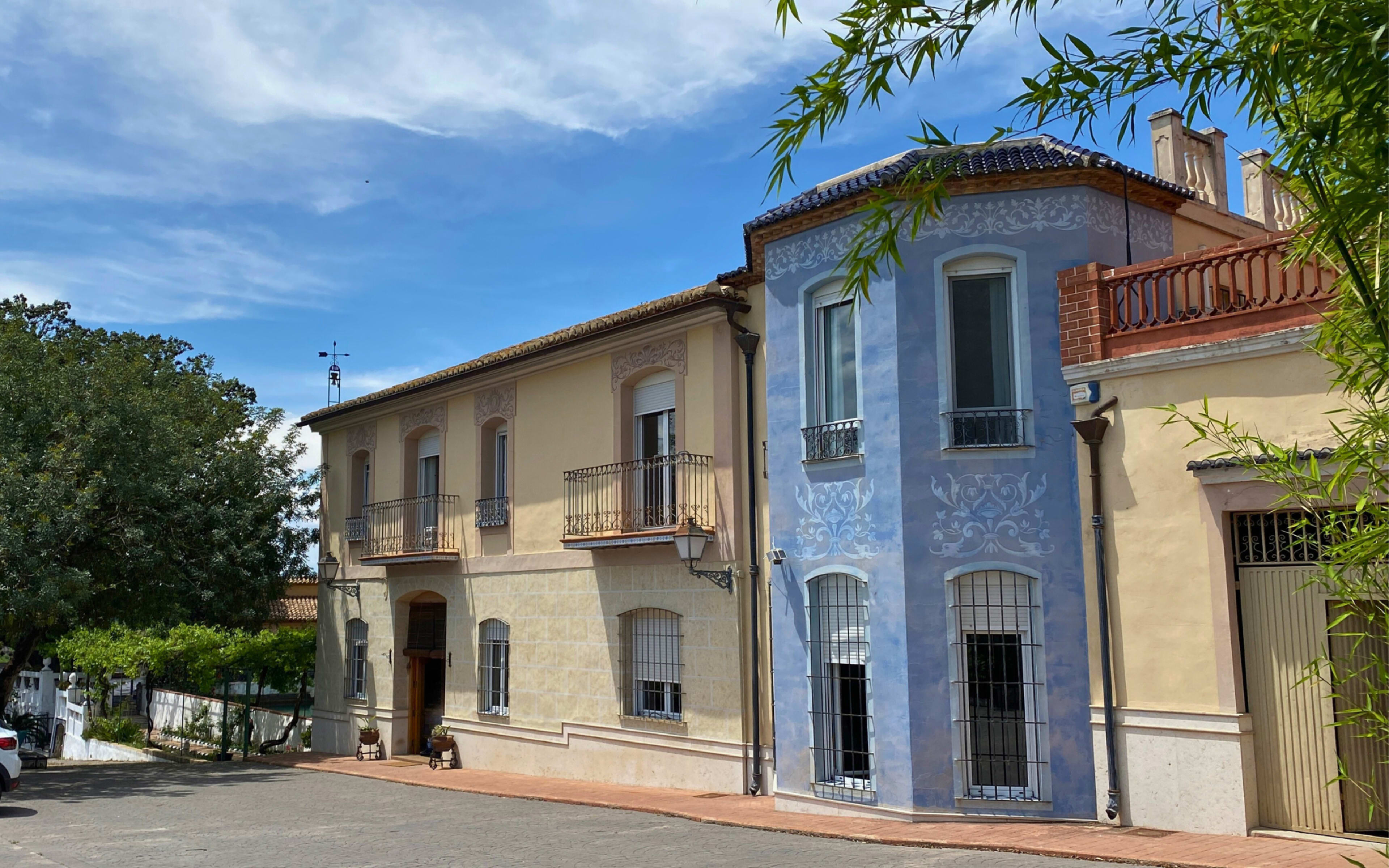 The image shows a picturesque street lined with colorful buildings, featuring a two-story house with a blue facade and decorative elements alongside a beige building.