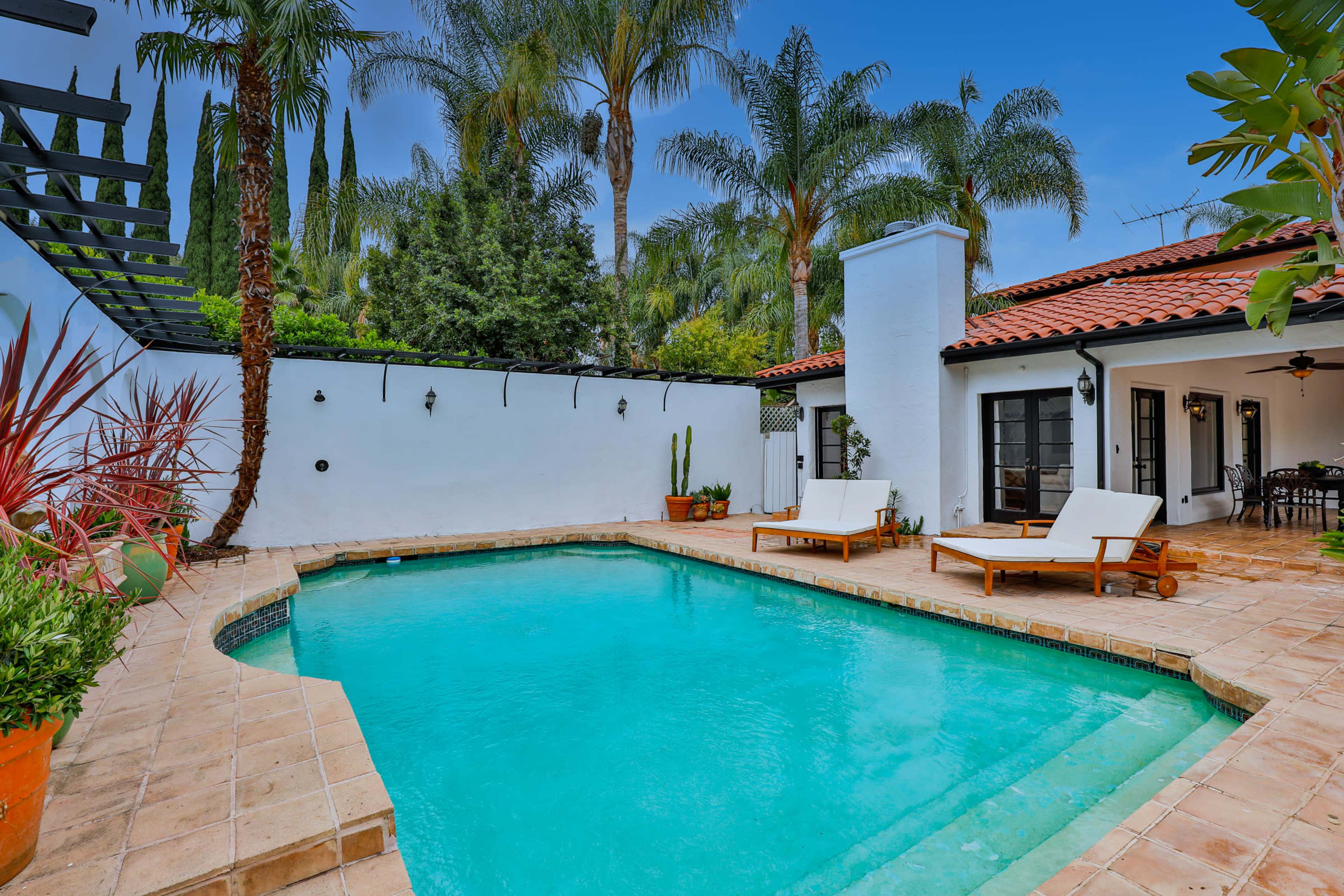 A residential backyard featuring a turquoise swimming pool surrounded by palm trees and lounge chairs.