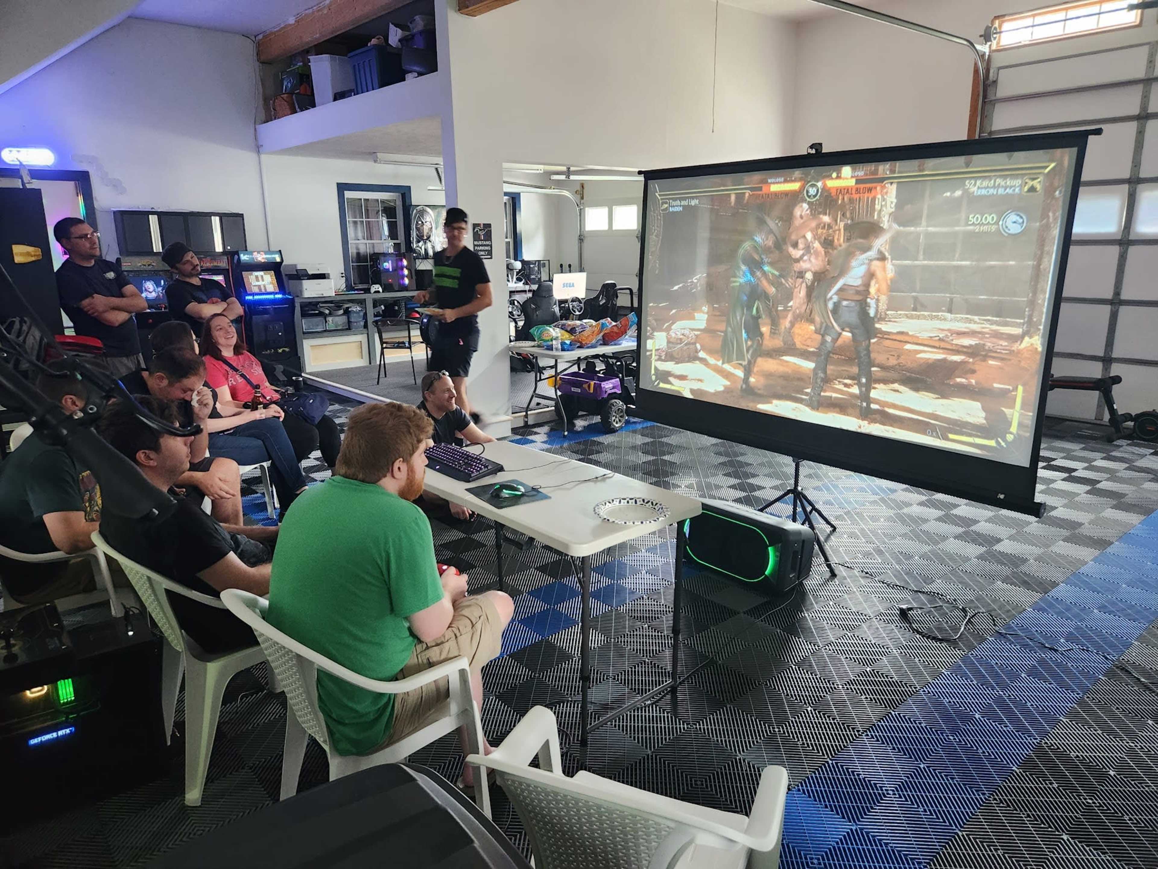 A group of people watches a video game match on a large screen in a gaming setup.