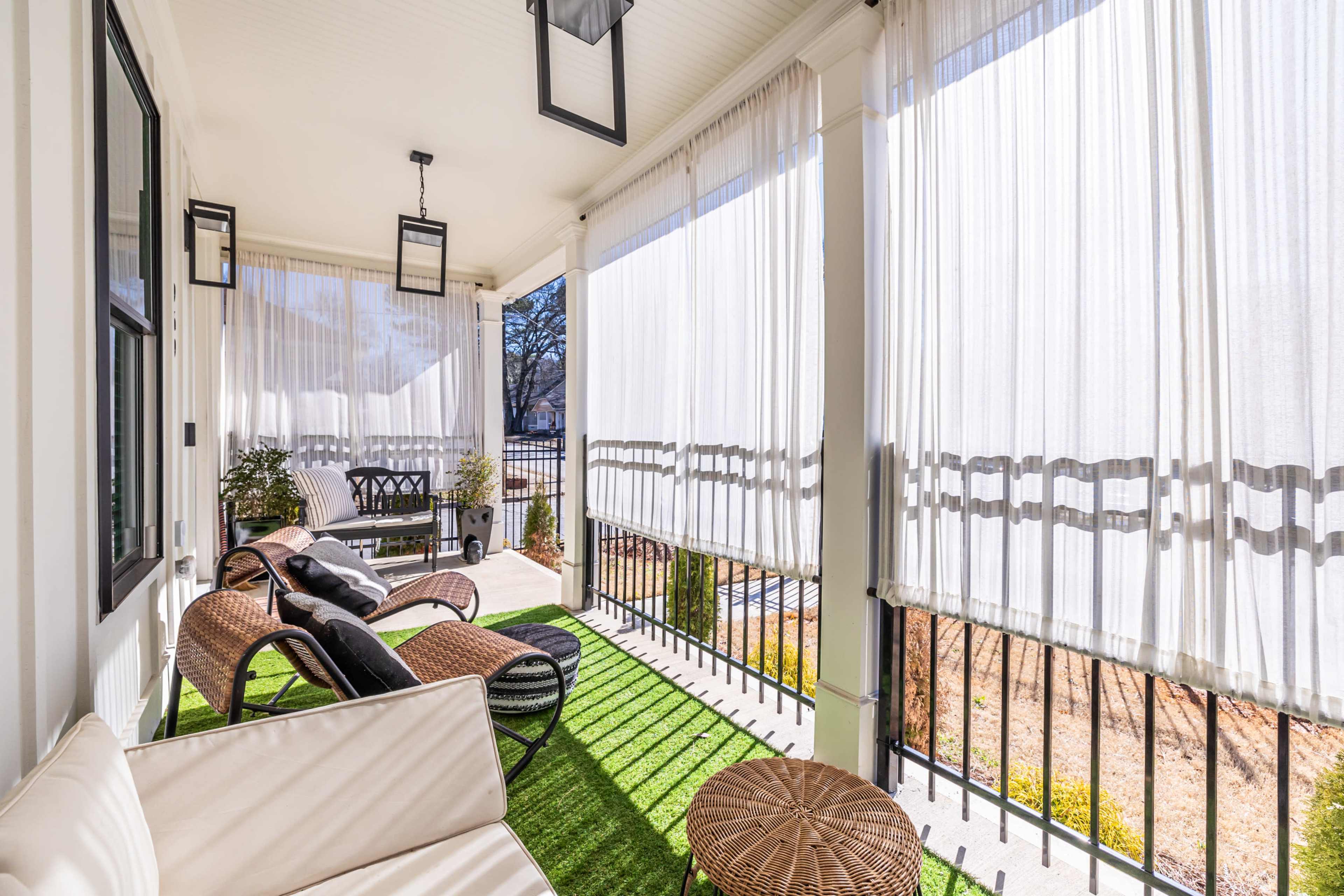 The image shows a covered porch featuring wicker furniture, decorative curtains, and artificial grass flooring.