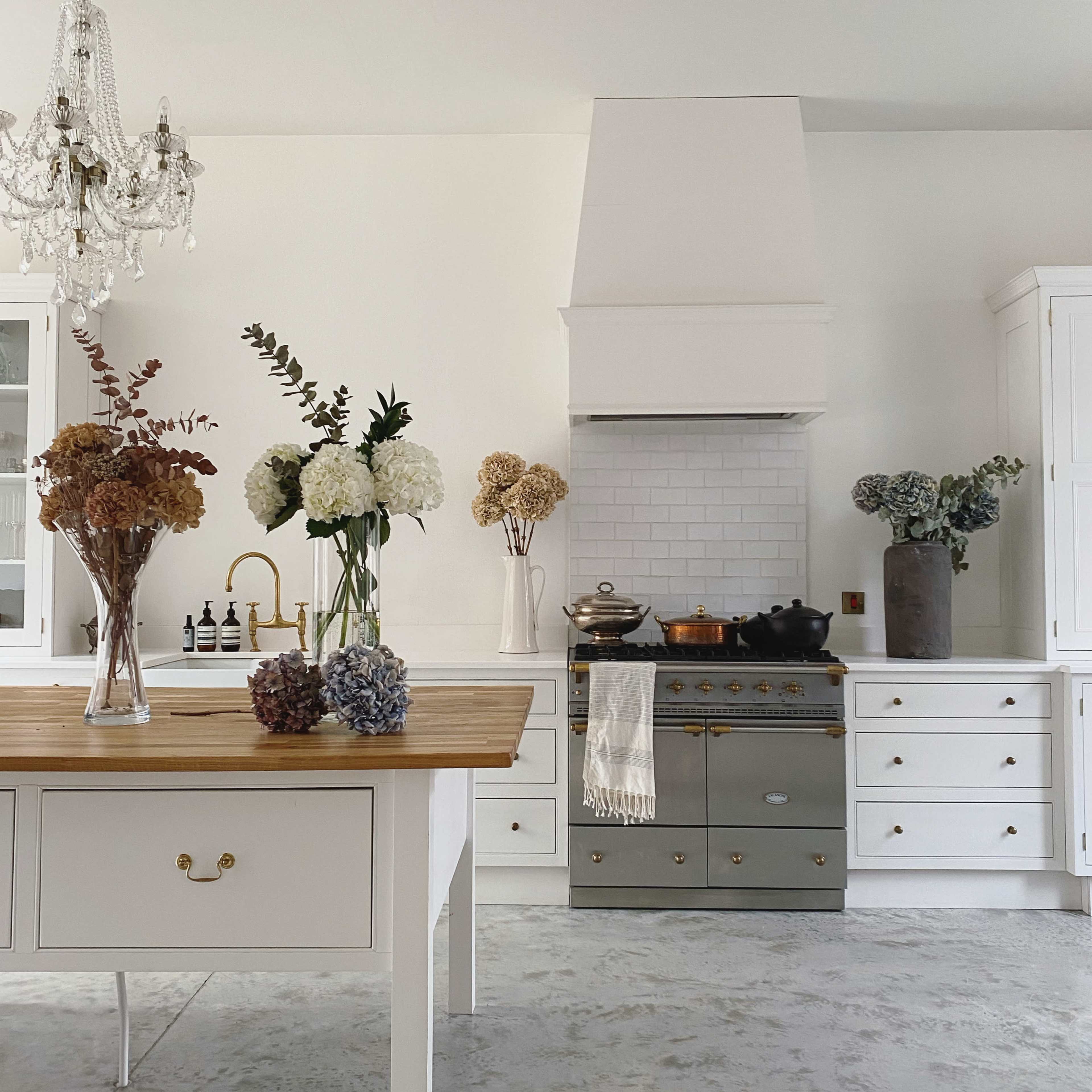 A modern kitchen features a central wooden island, a vintage-style stove, and various vases of flowers on the counters.