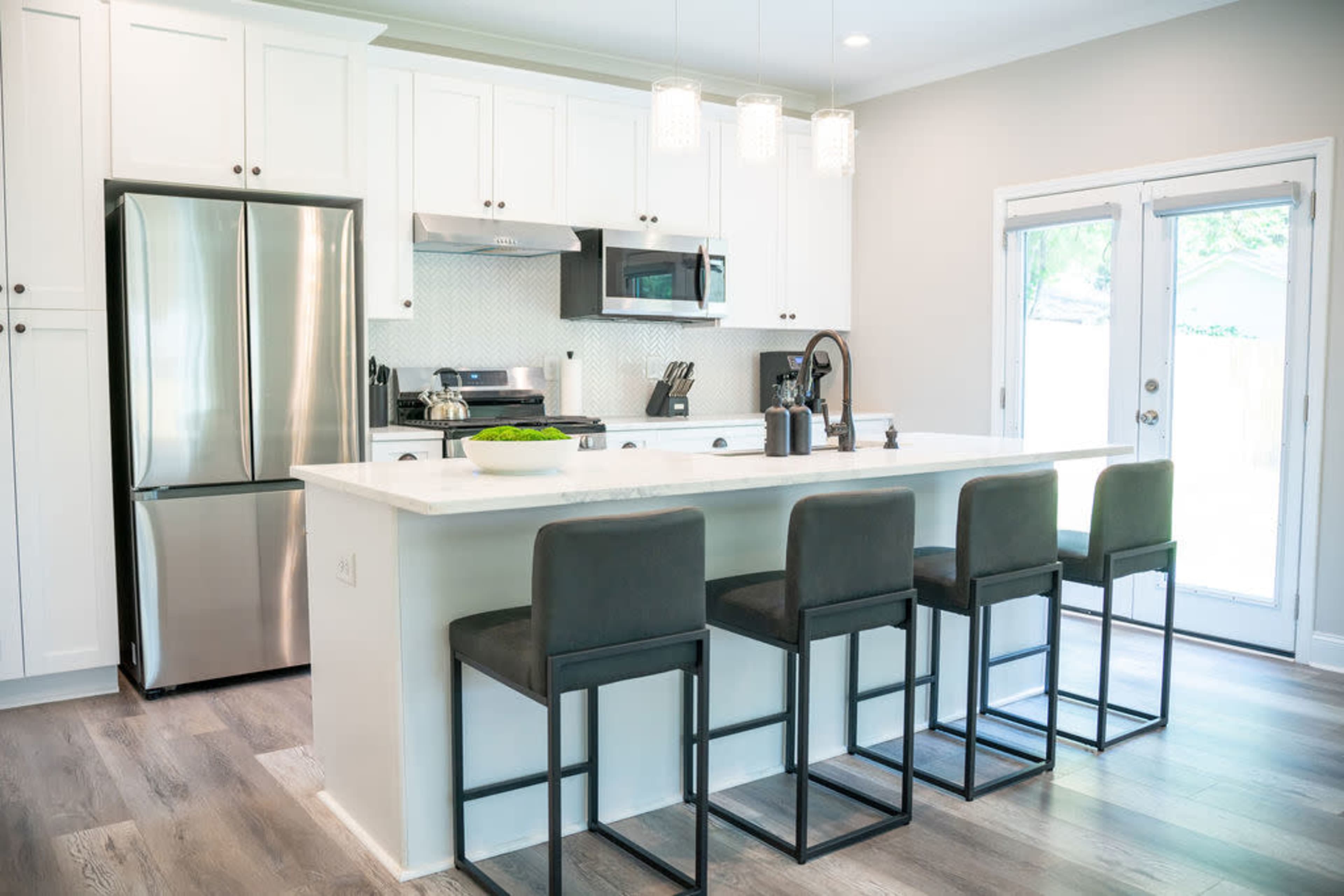 A modern kitchen features white cabinetry, stainless steel appliances, a large island with seating for four, and sliding glass doors leading to an outdoor area.