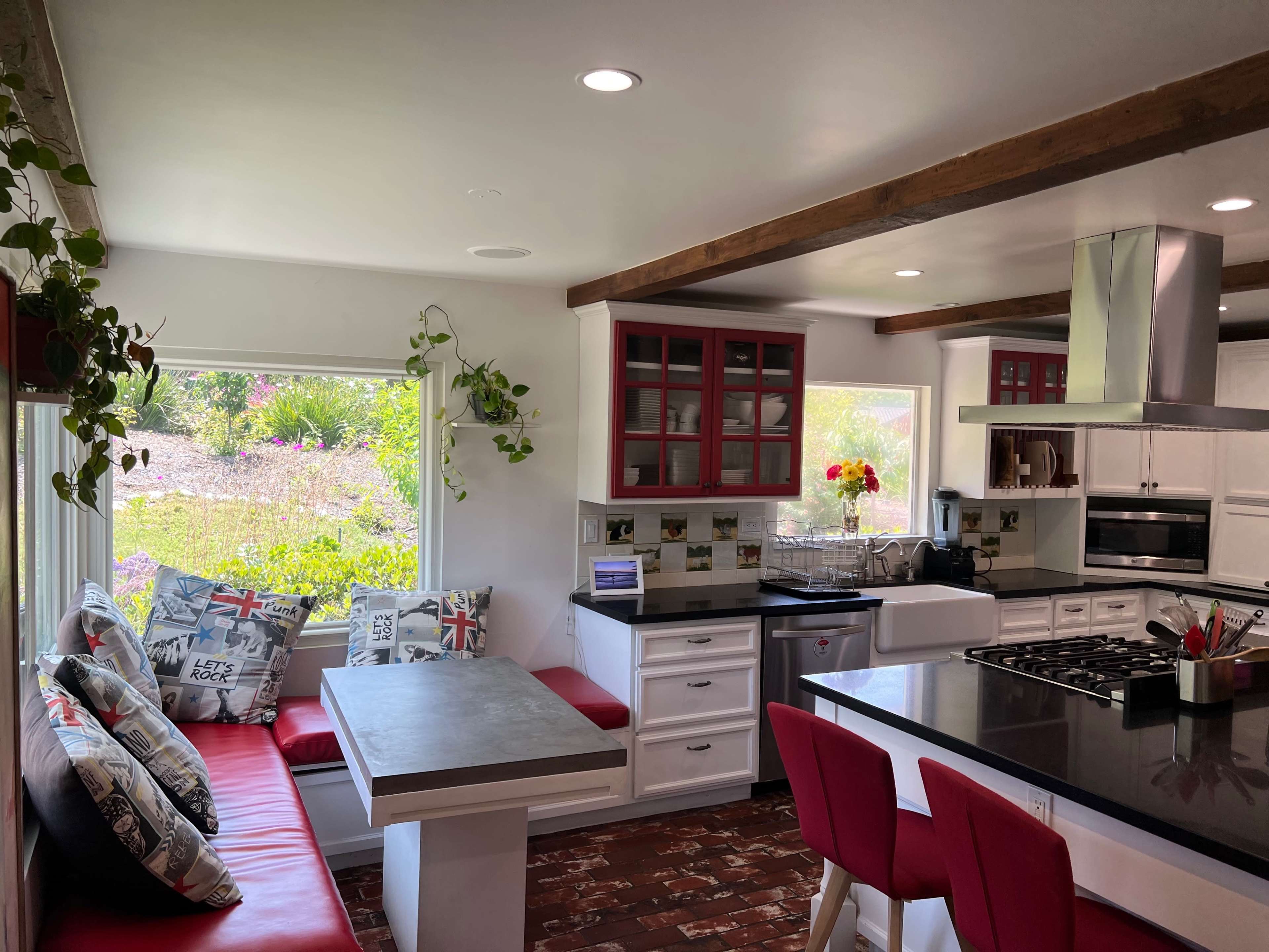 A modern kitchen features a red and white color scheme with a dining area, a central island, and large windows overlooking greenery.