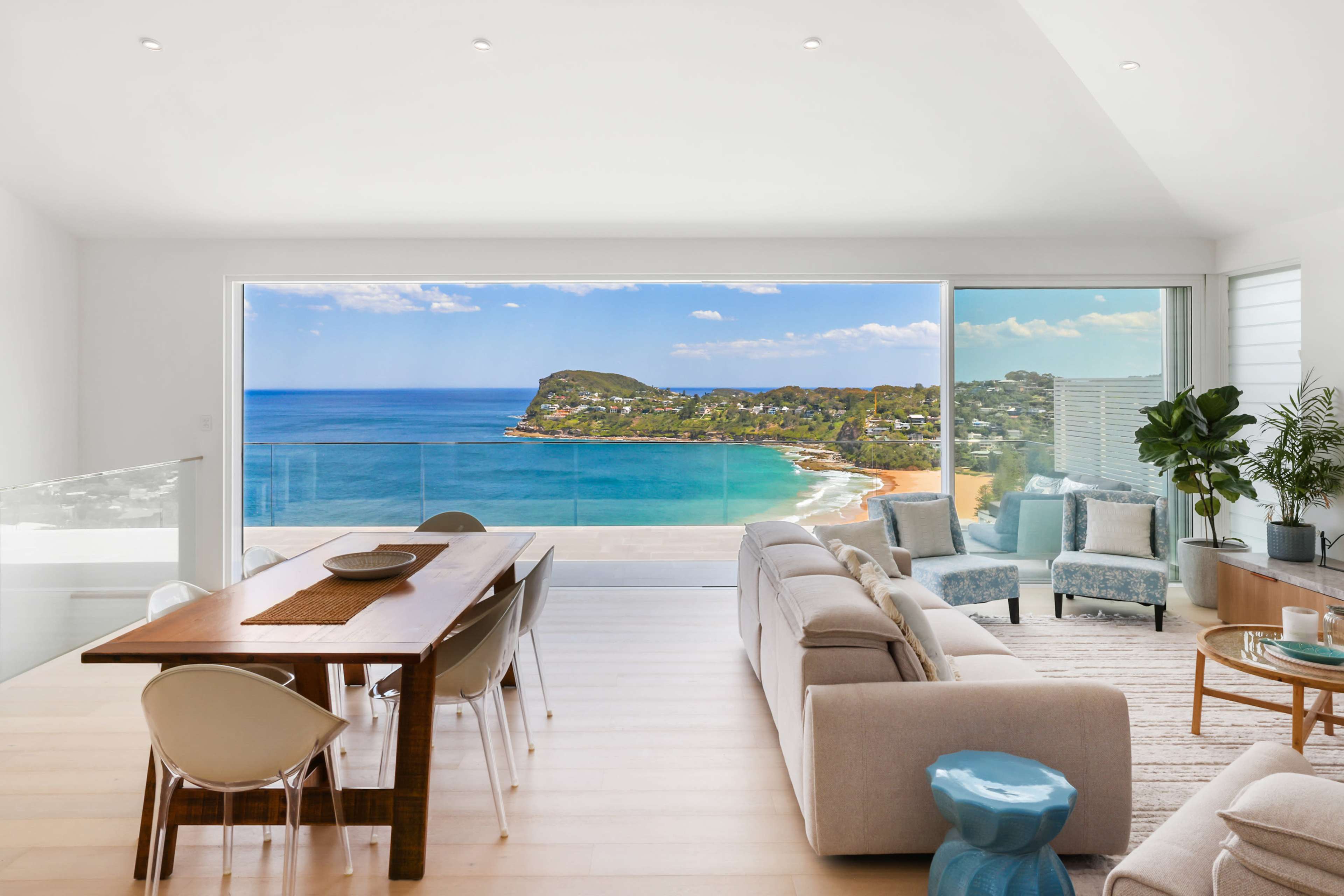 A modern living space with a view of the ocean and a coastal landscape through large glass windows.