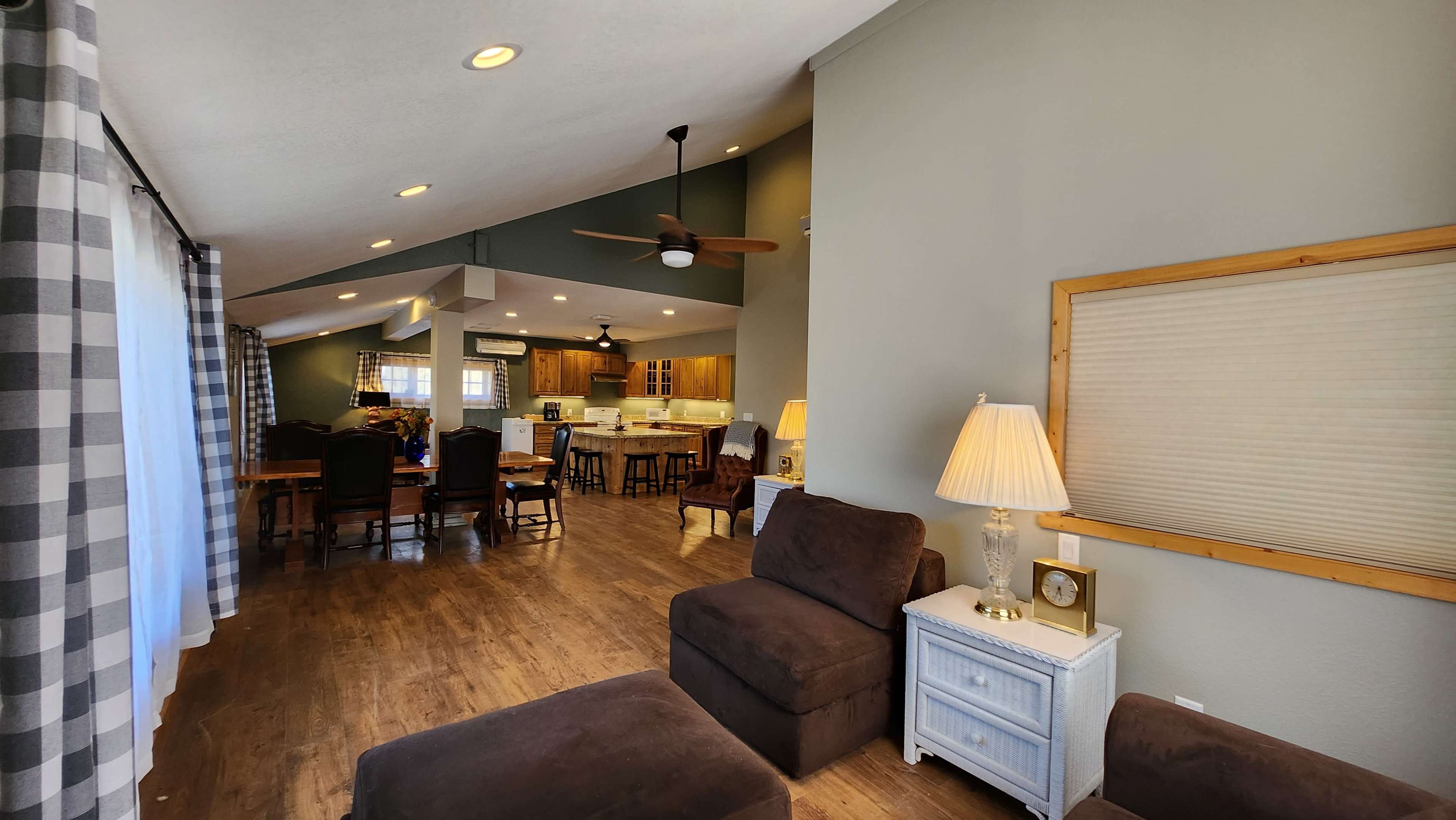A spacious living area with dark furniture, a ceiling fan, and an open kitchen visible in the background.