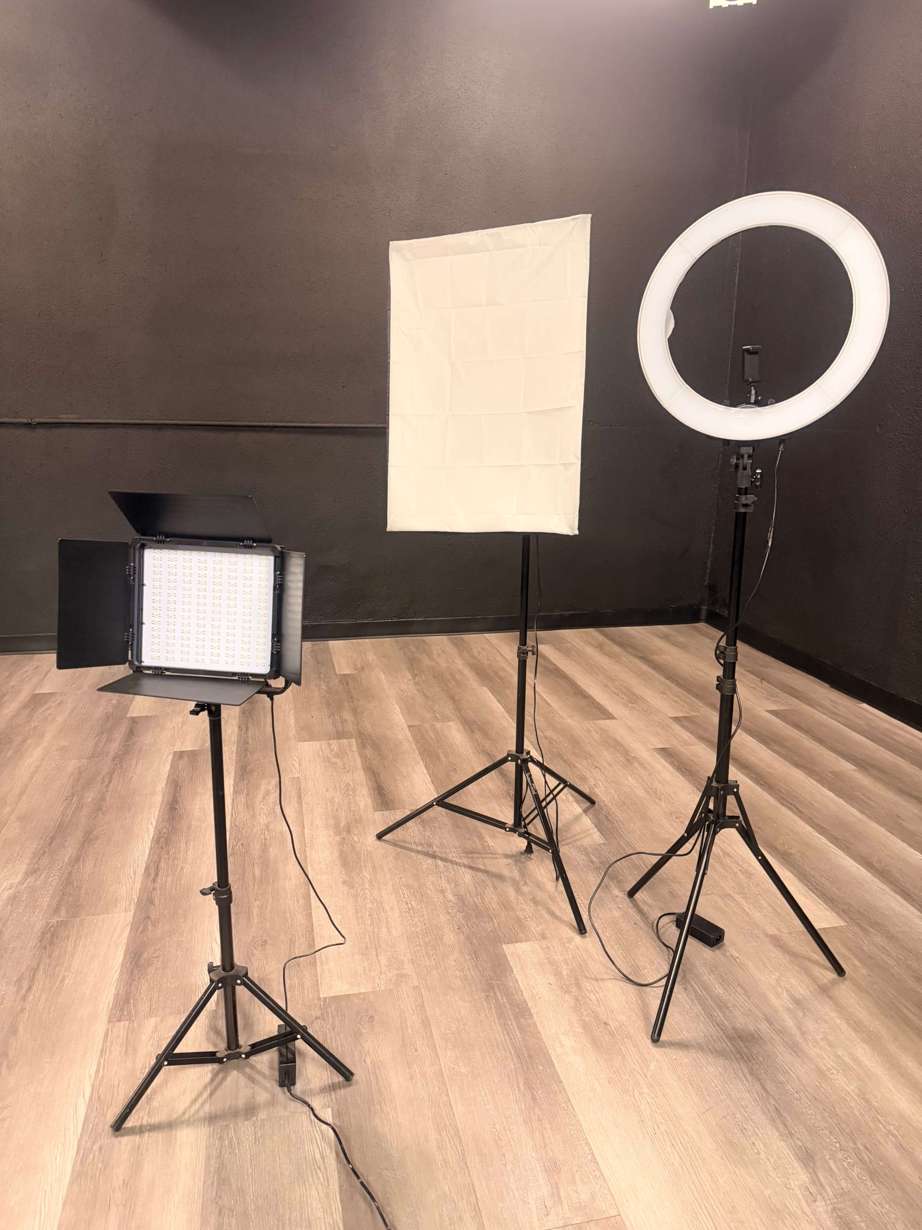 The image shows three lighting equipment setups in a studio, including a softbox, a ring light, and an LED panel, all positioned on tripods.