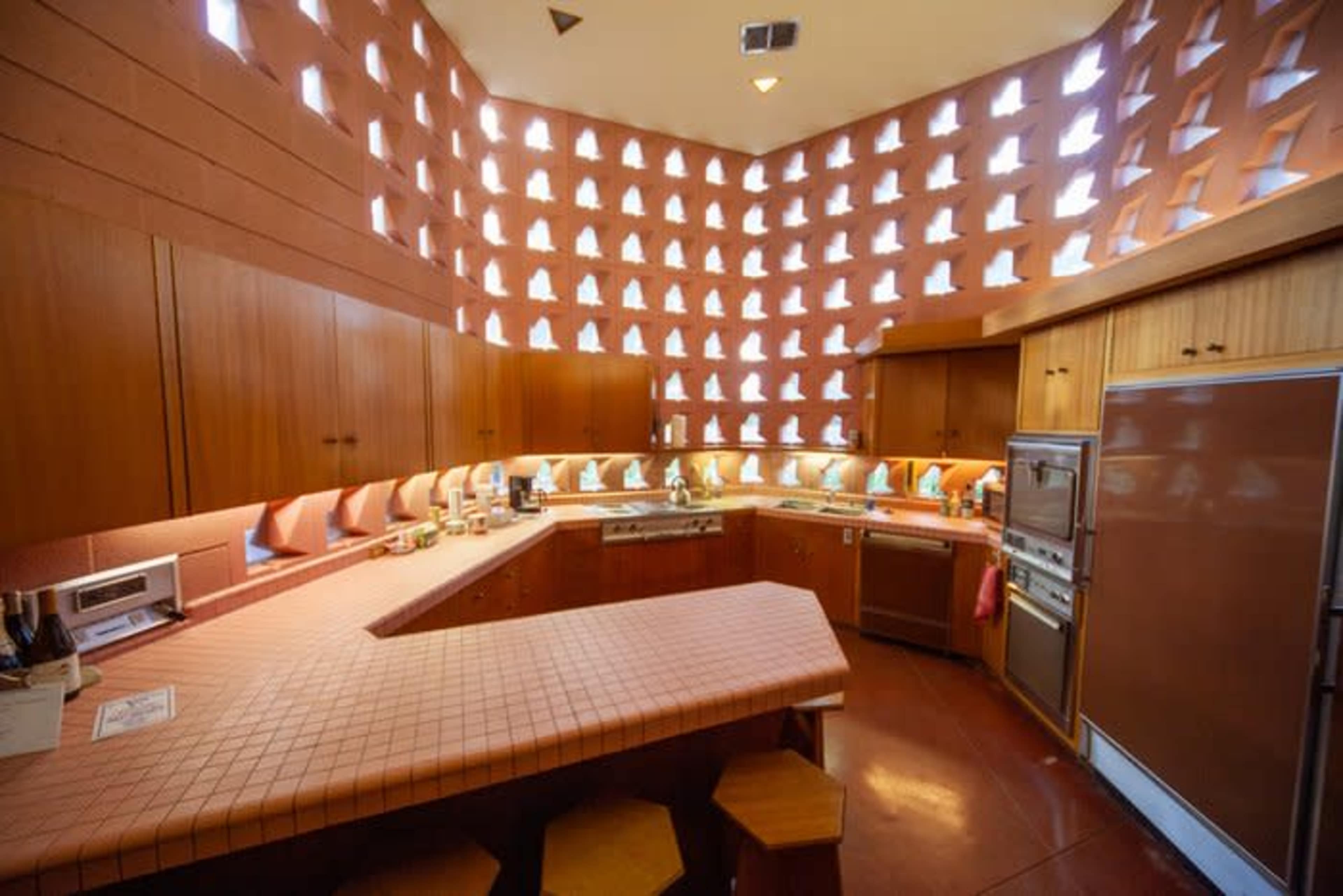 The kitchen features a unique design with an angled counter, brown cabinetry, and multiple small windows creating a patterned light effect on the walls.