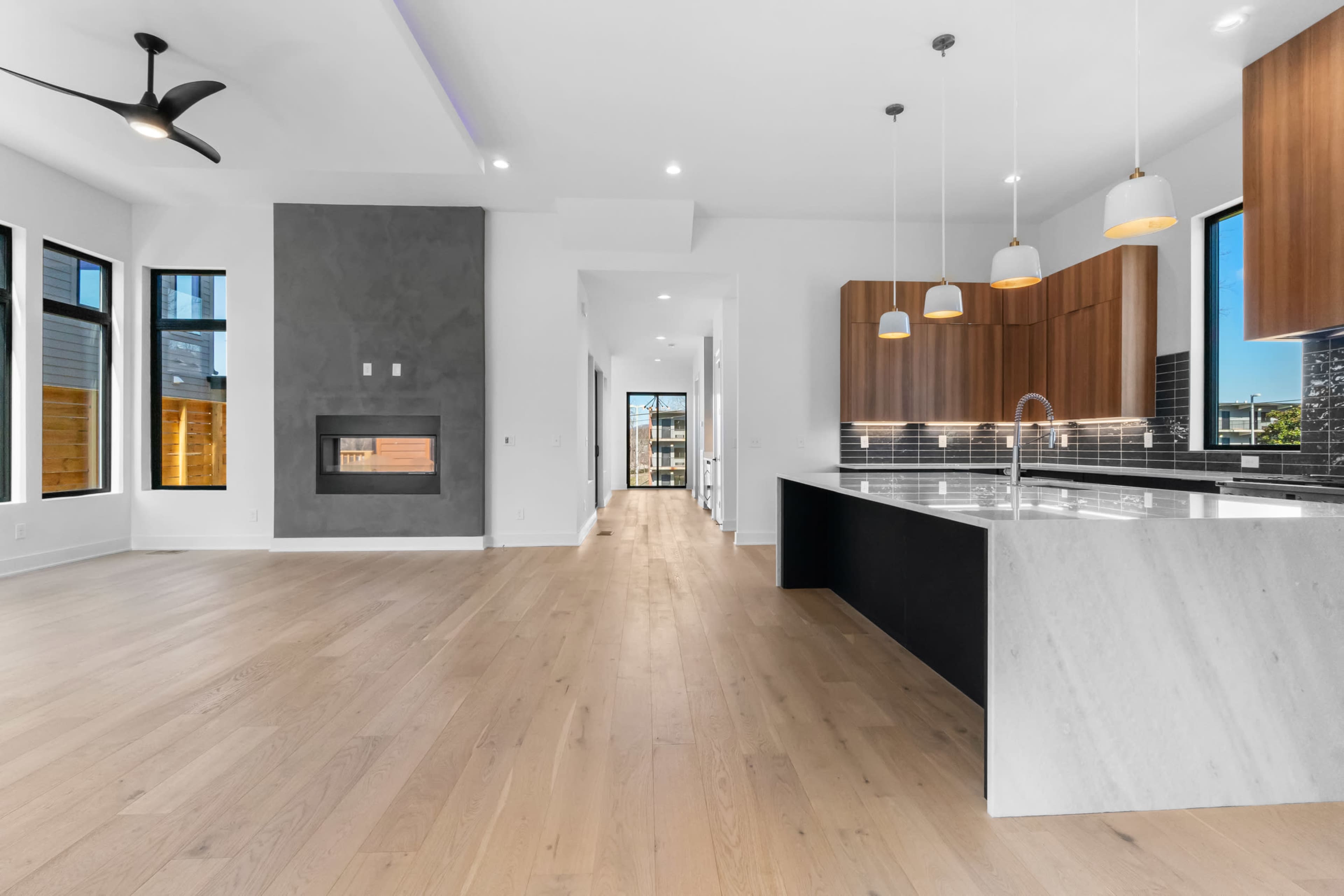 The image shows a modern open-concept living space featuring a kitchen with a large island, a dining area, and a fireplace, all adorned with large windows for natural light.