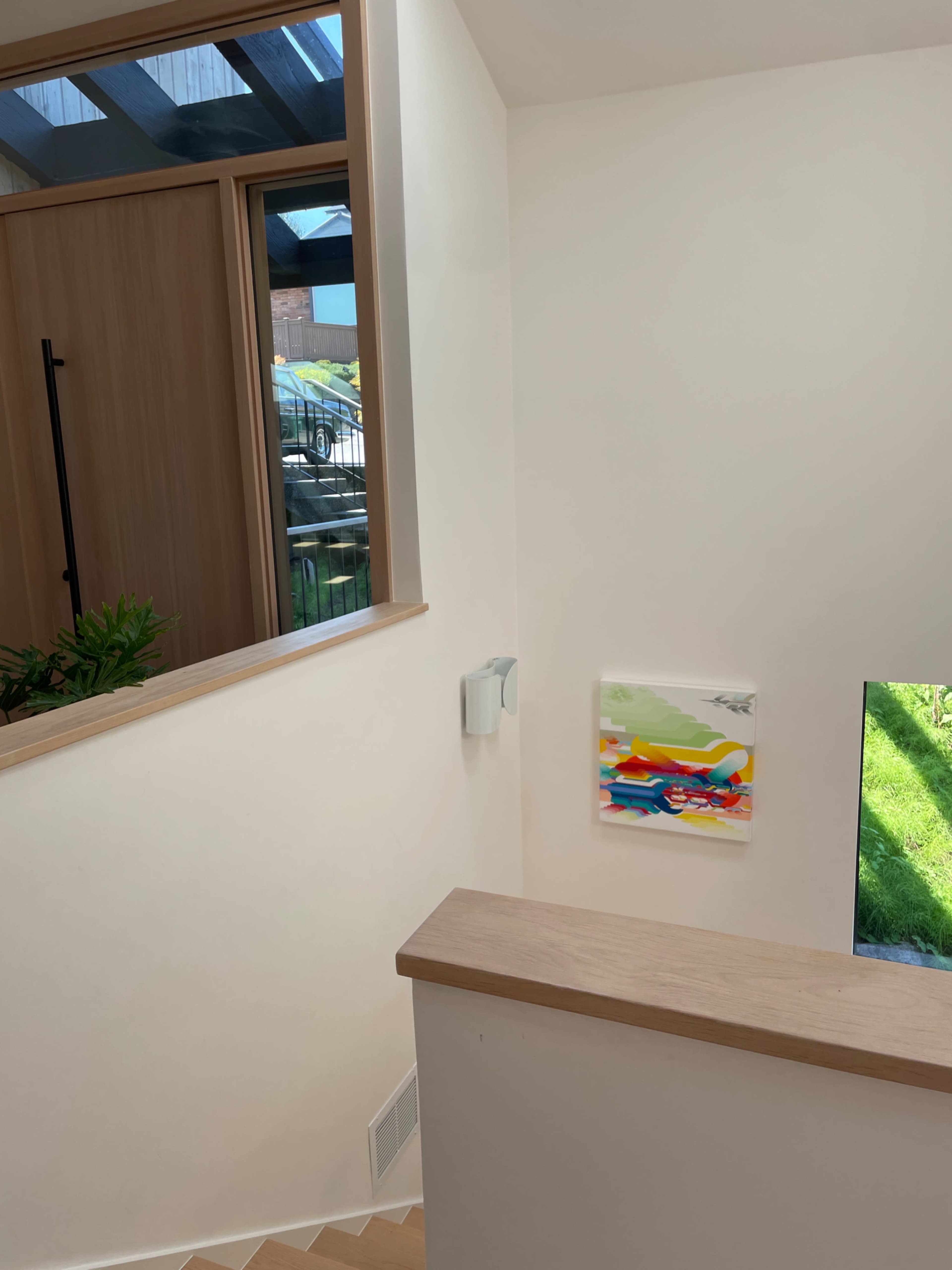 A staircase leads down to a landing with a colorful painting on the wall and a view of greenery outside through a window.