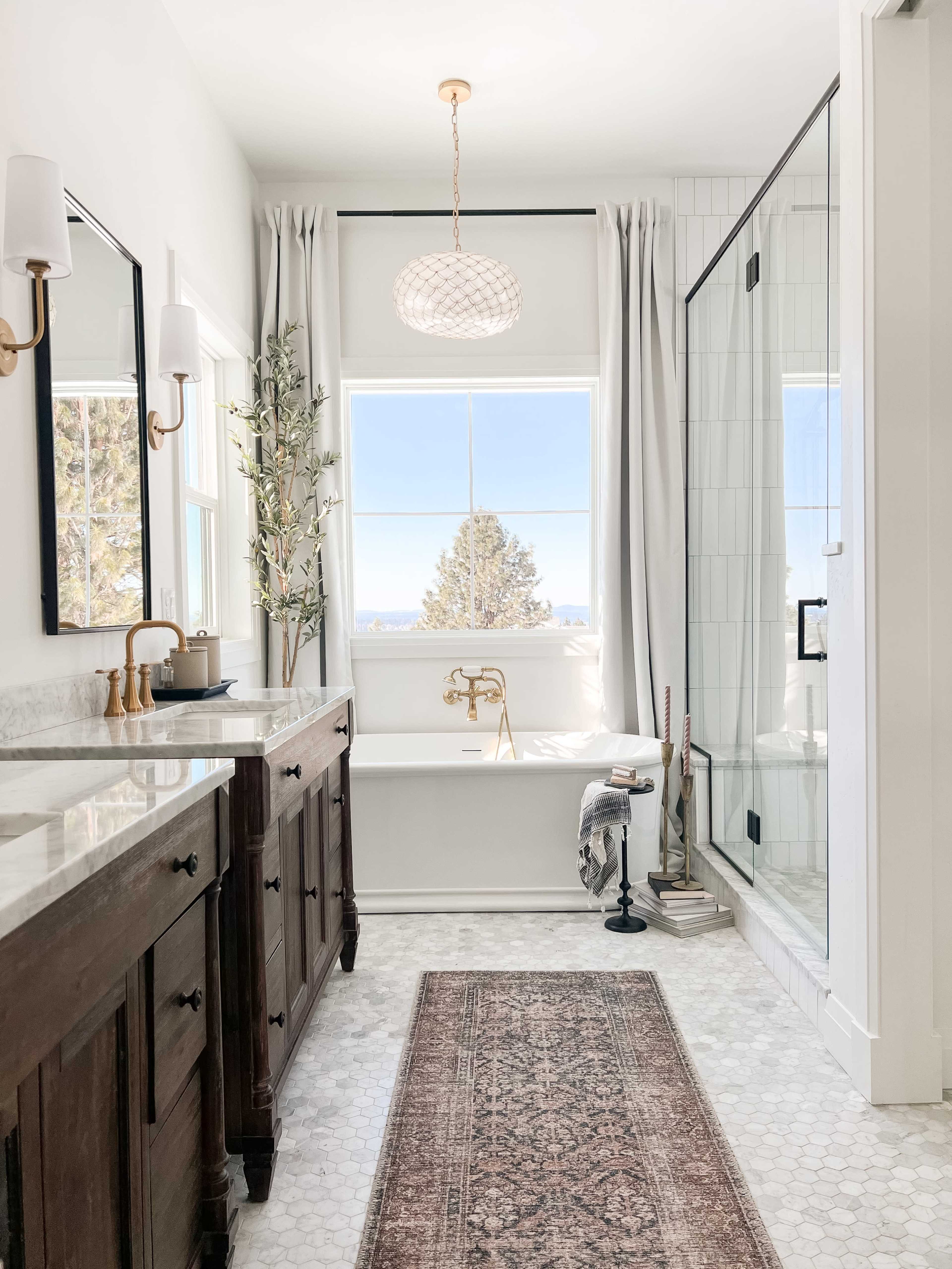 The bathroom features a tub near a large window, a glass shower enclosure, and double sinks with wooden cabinetry.