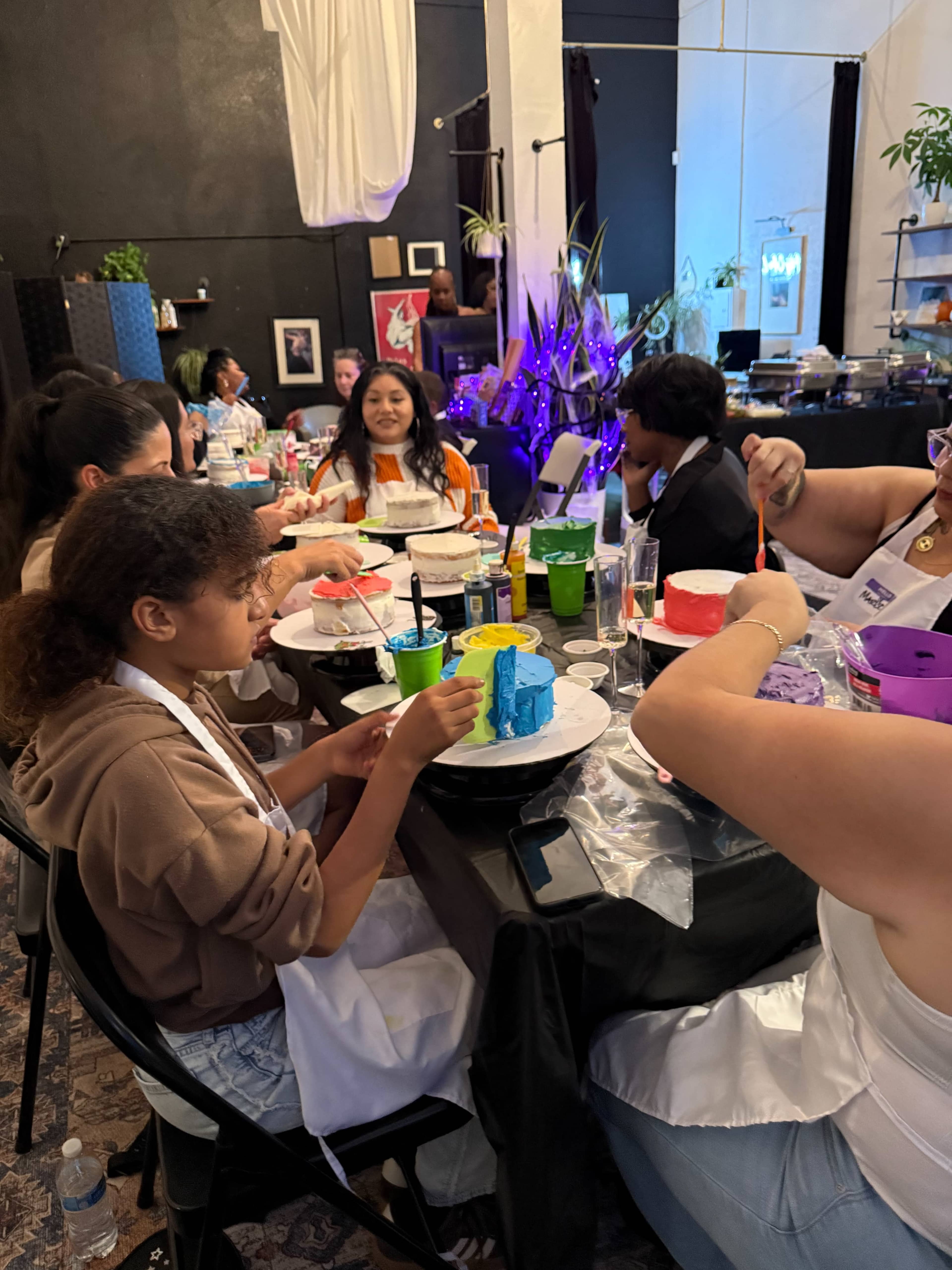 A group of people sits at a table, painting colorful ceramic pieces during an art workshop.