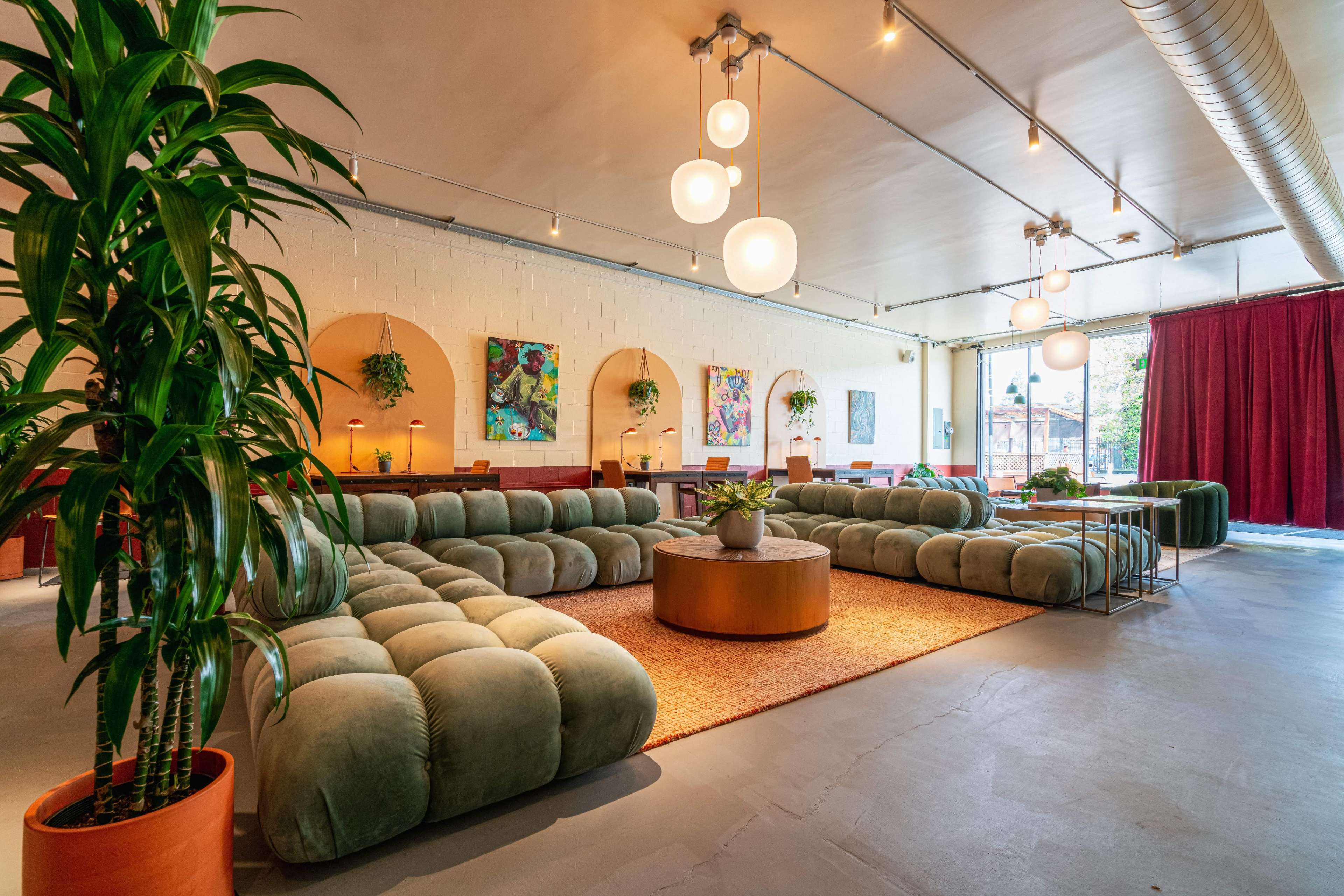 A spacious interior lounge area featuring large, green cushioned seating arrangements, potted plants, and modern lighting fixtures.