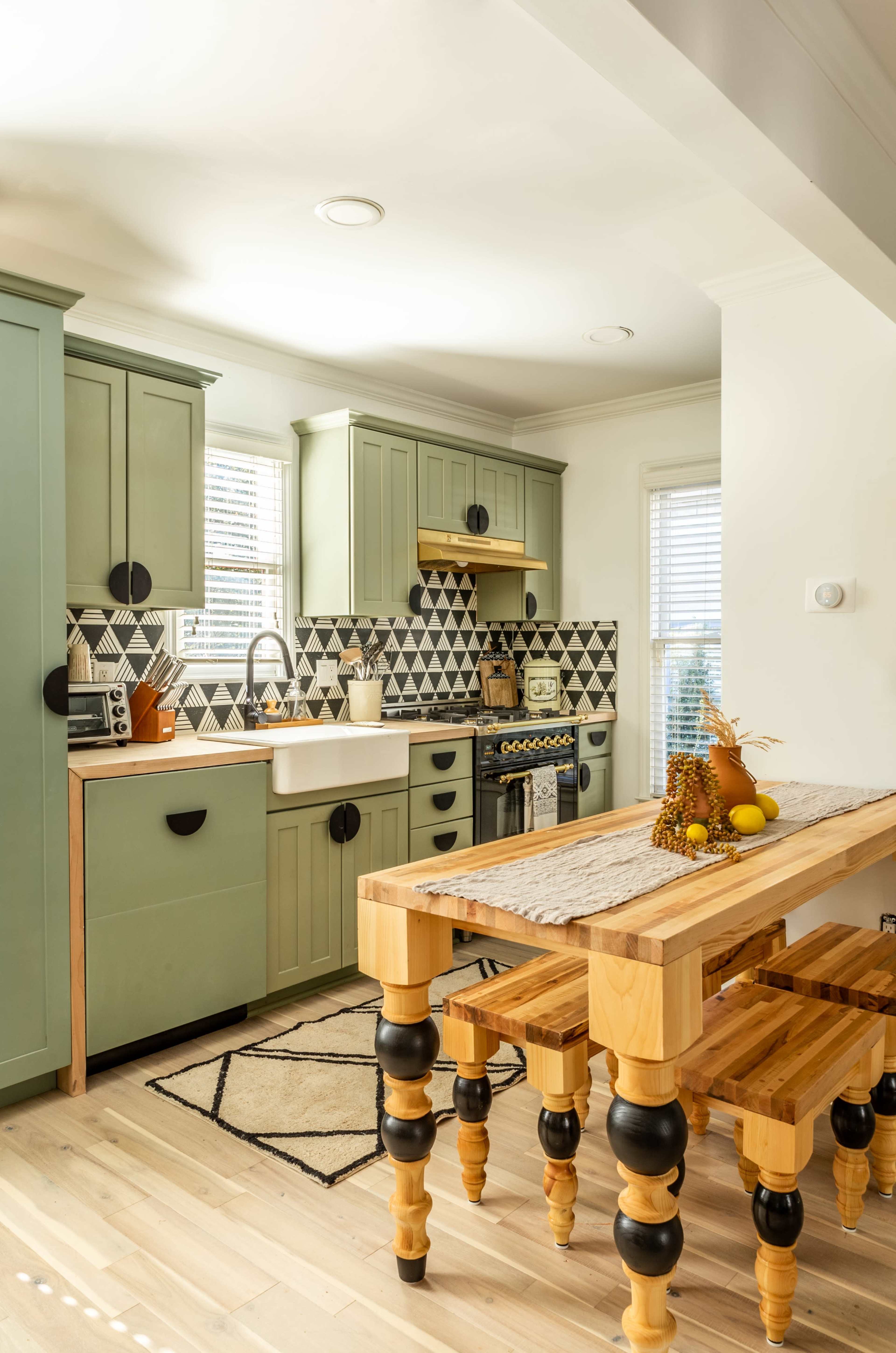 The kitchen features green cabinets, a patterned backsplash, and a wooden dining table with black legs.
