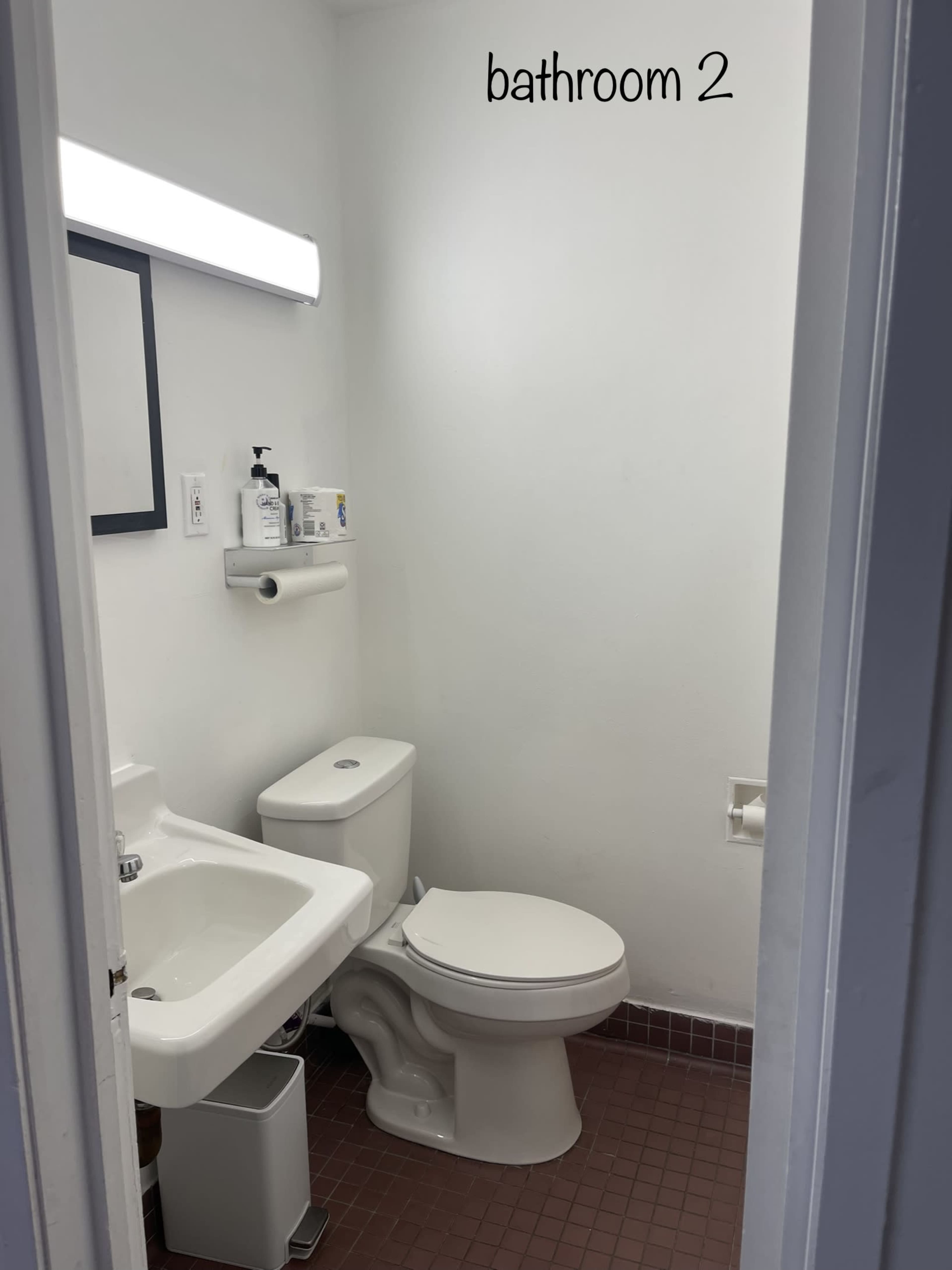 A small bathroom featuring a toilet, a sink, a wall-mounted mirror, and a light fixture above the sink.