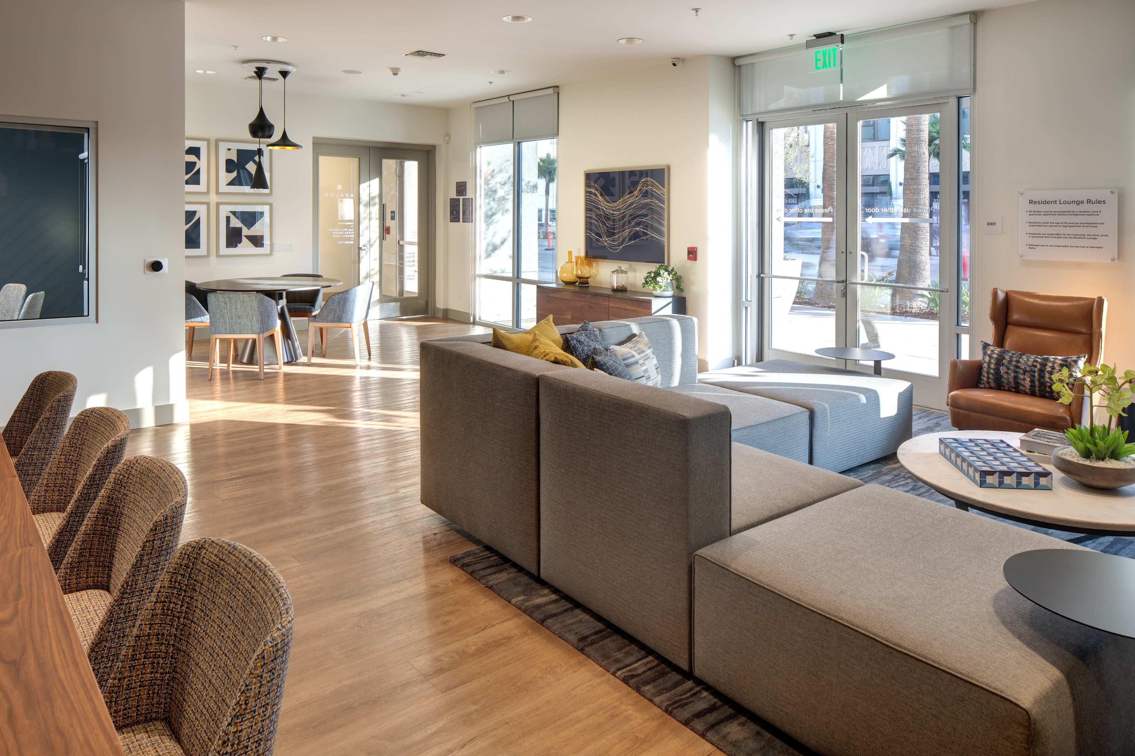 A modern lounge area with a sectional sofa, wooden furniture, and large windows letting in natural light.