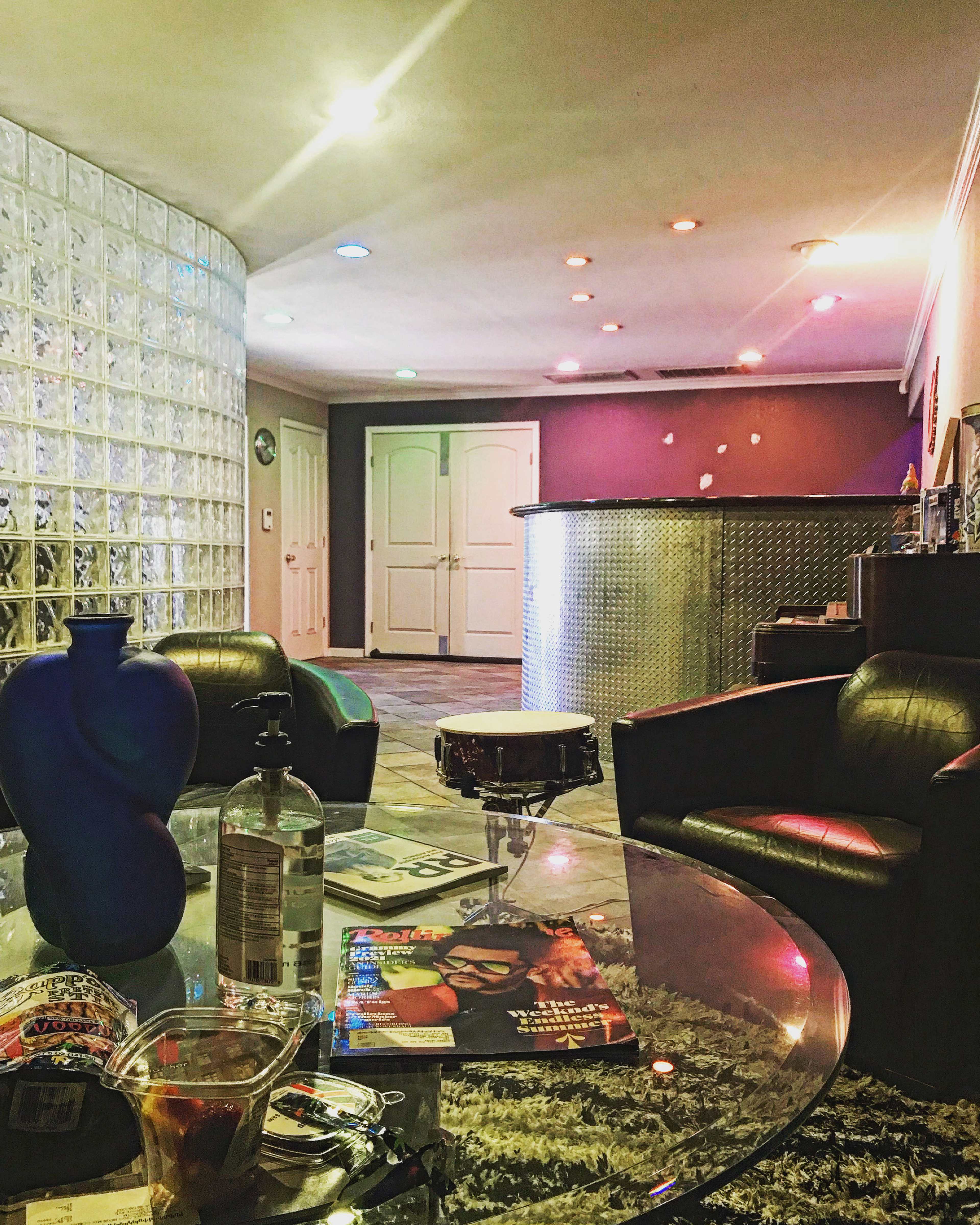 The scene shows a modern interior featuring a glass block wall, a circular bar area, and a coffee table with drinks and magazines in a lounge setting.