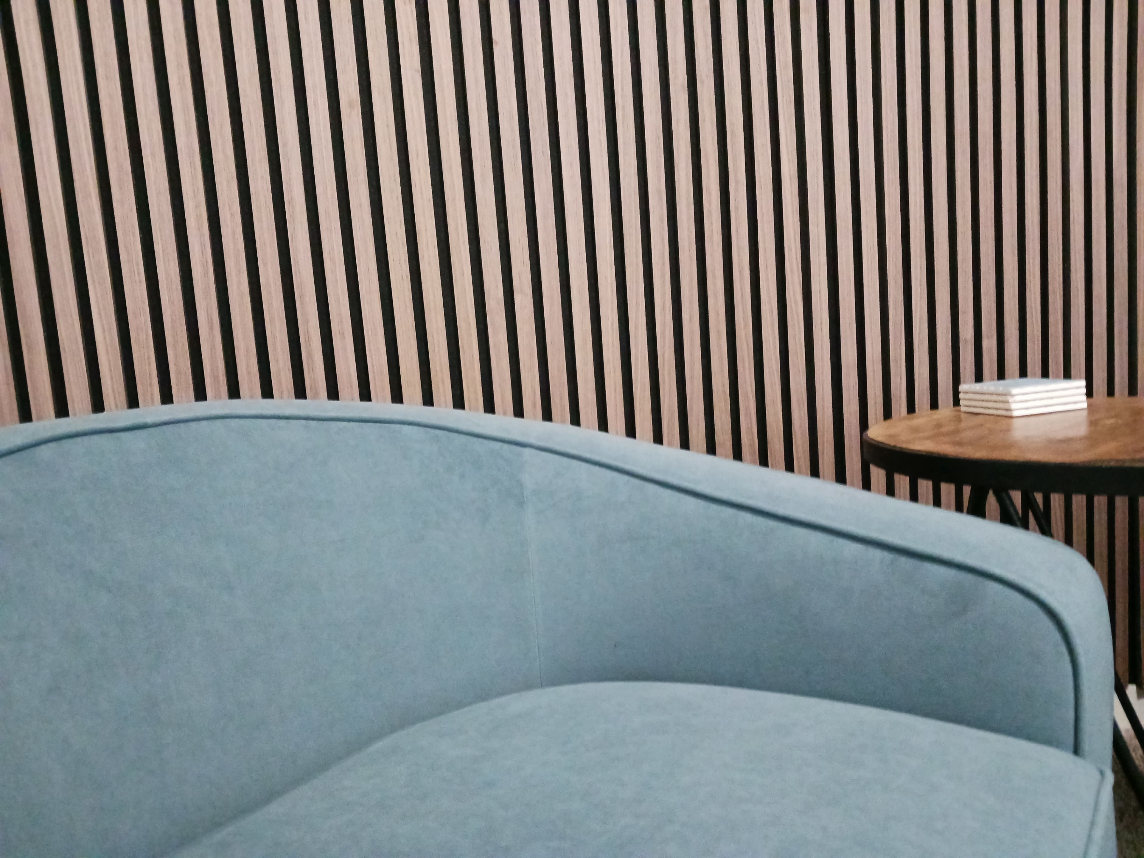 A light blue upholstered sofa is positioned next to a round wooden table, against a backdrop of vertical wooden slats.