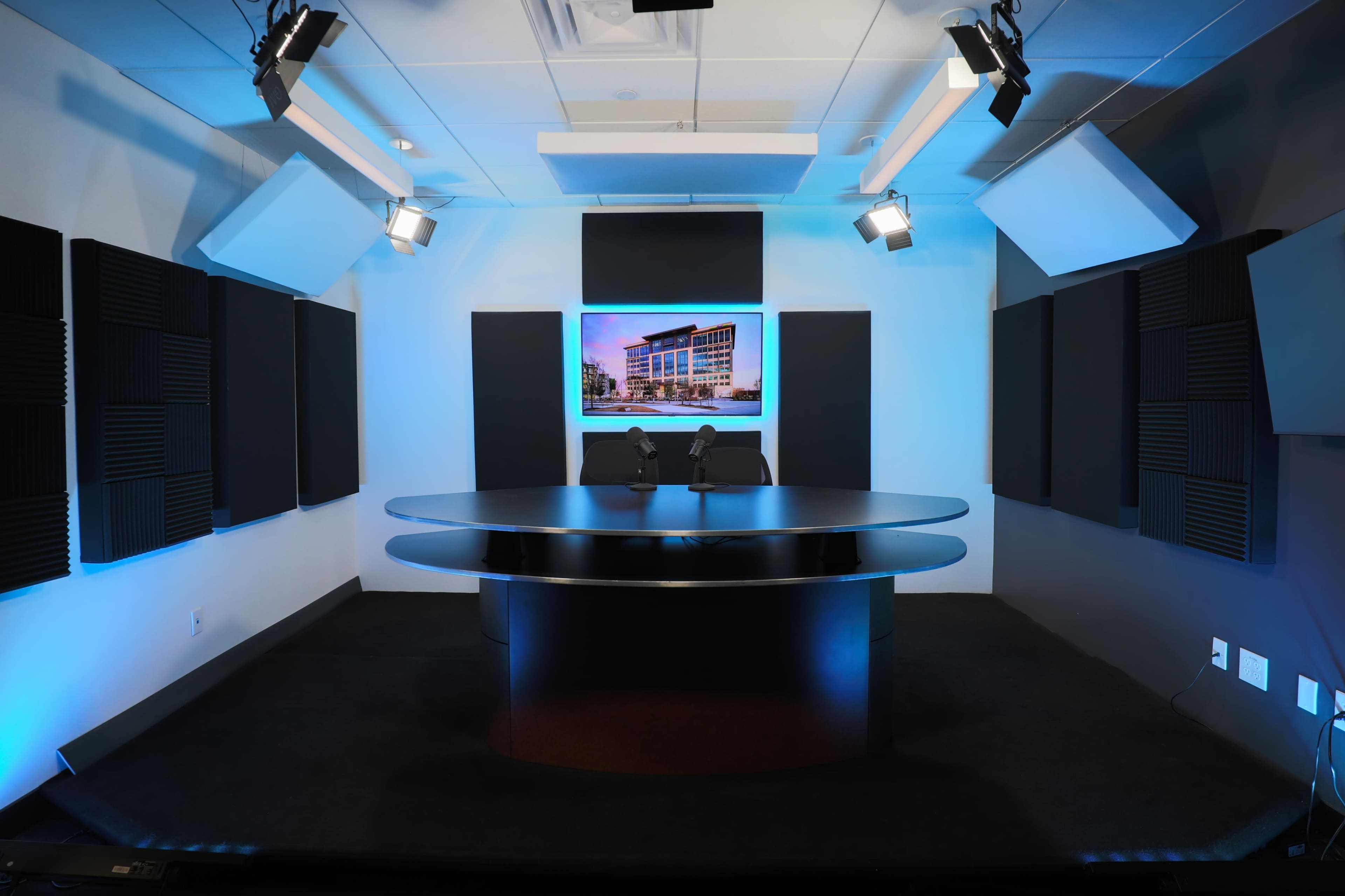 A modern conference room with a circular black table, two chairs, and soundproof walls, featuring a large screen displaying a building image.